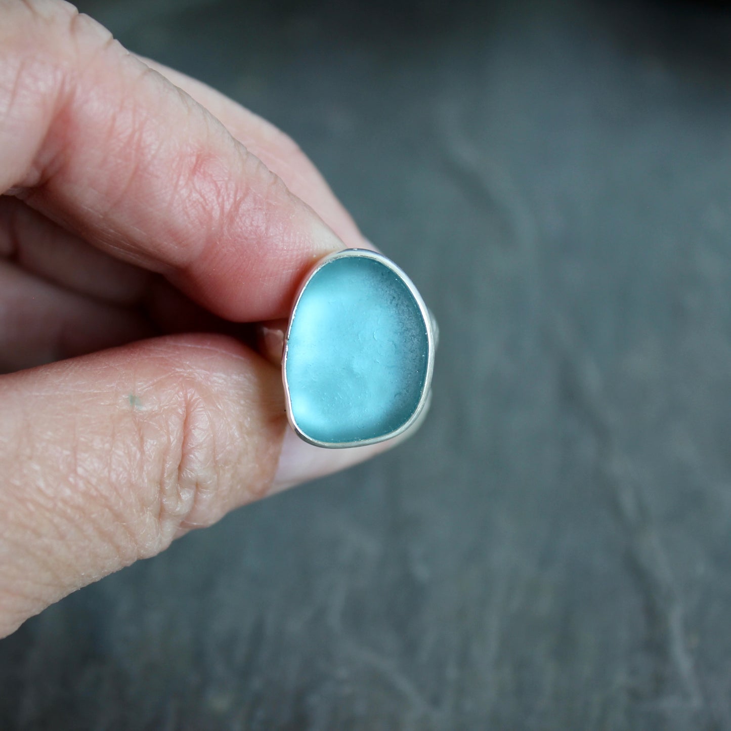 This ring has a large piece of aqua turquoise blue sea glass that is set in a fine and sterling silver bezel setting on a sturdy wide hammered band.  Size 4 1/2 Handmade by Barb Macy in Corvallis, Oregon.