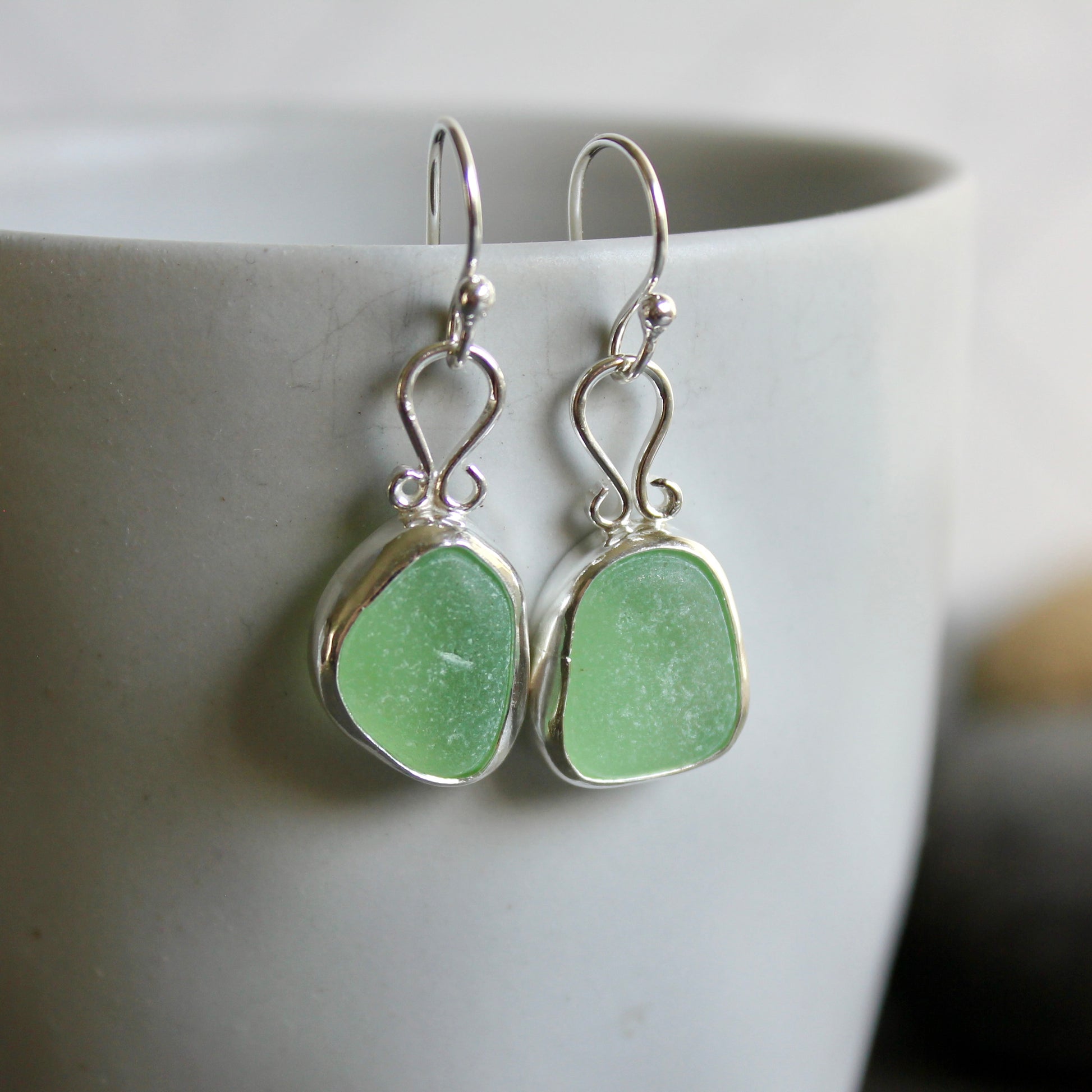 These earrings have two pieces of mint sea foam green sea glass from Massachusetts (USA). They are set in a sterling and fine silver bezel setting and are on sterling silver ear wires. All of our sea glass is found and not altered in any way. Handmade by Barb Macy in Corvallis, OR. 
