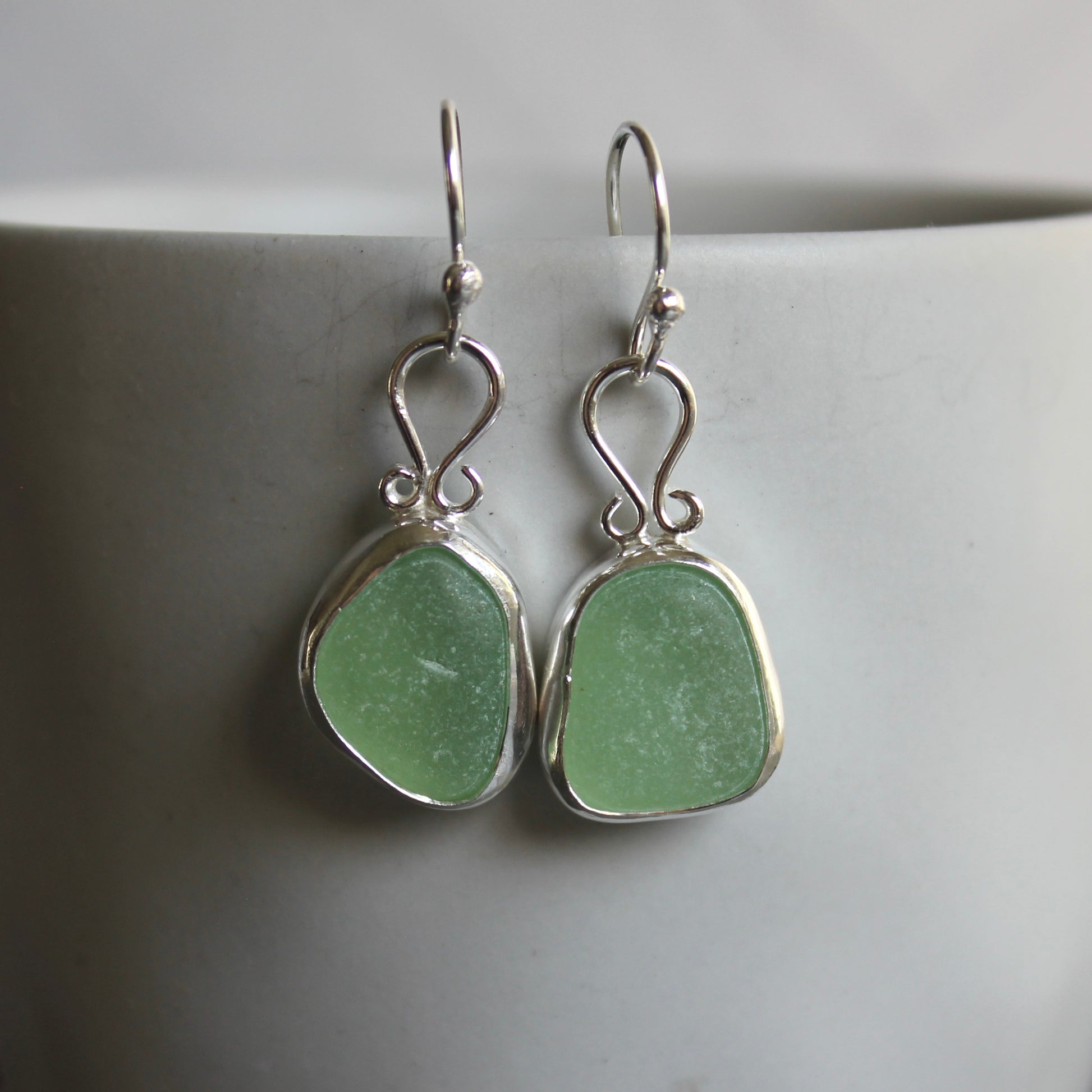 These earrings have two pieces of mint sea foam green sea glass from Massachusetts (USA). They are set in a sterling and fine silver bezel setting and are on sterling silver ear wires. All of our sea glass is found and not altered in any way. Handmade by Barb Macy in Corvallis, OR. 
