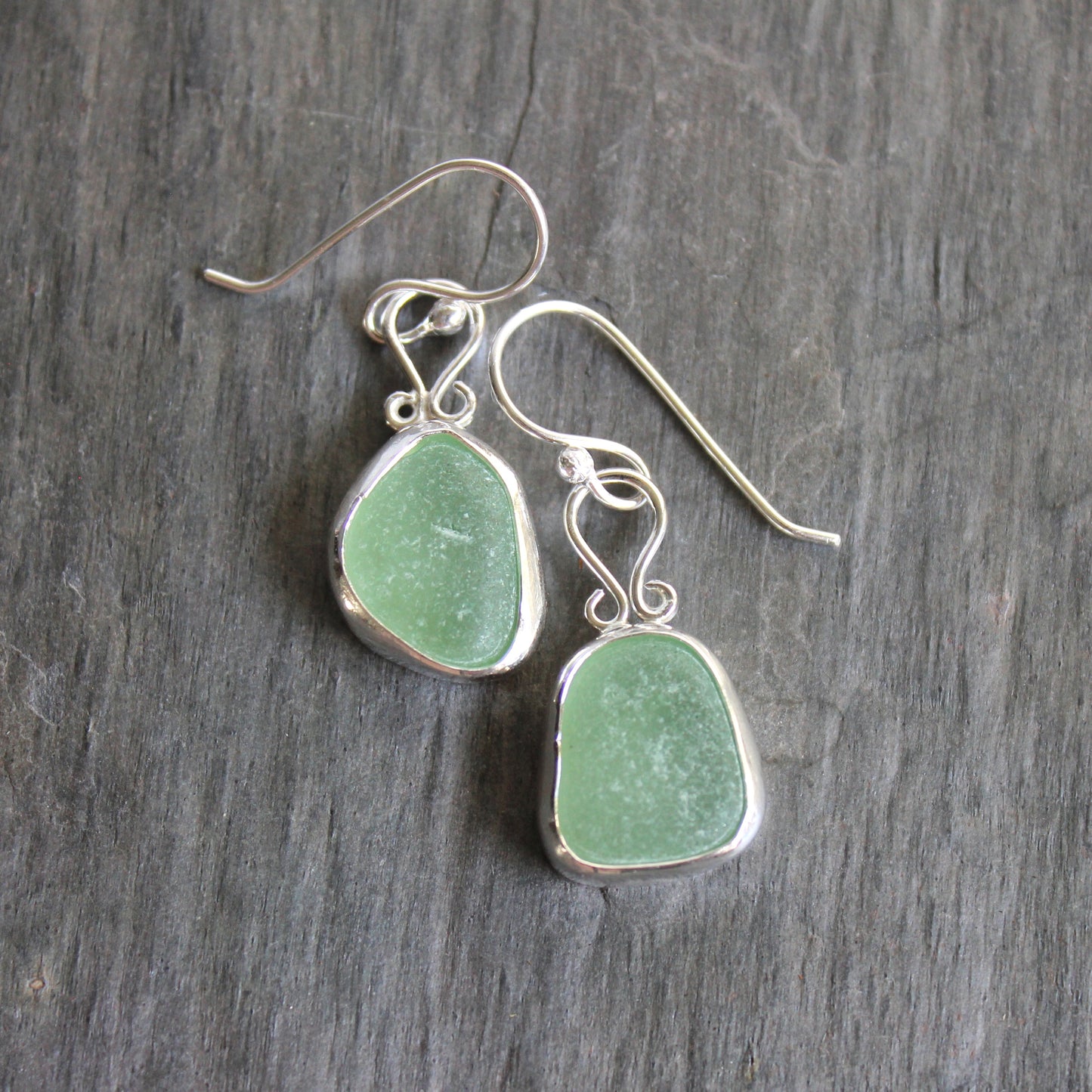 These earrings have two pieces of mint sea foam green sea glass from Massachusetts (USA). They are set in a sterling and fine silver bezel setting and are on sterling silver ear wires. All of our sea glass is found and not altered in any way. Handmade by Barb Macy in Corvallis, OR. 
