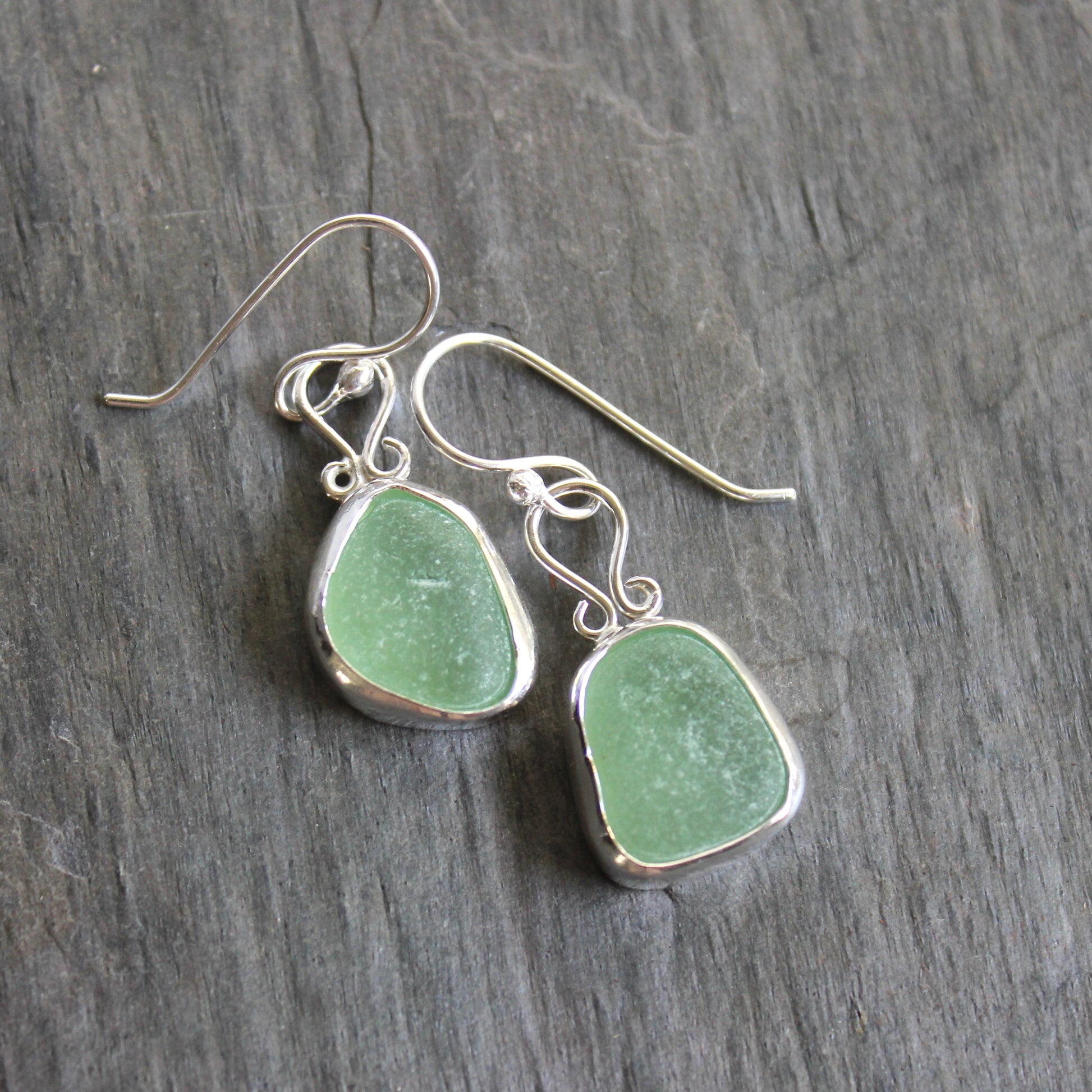 These earrings have two pieces of mint sea foam green sea glass from Massachusetts (USA). They are set in a sterling and fine silver bezel setting and are on sterling silver ear wires. All of our sea glass is found and not altered in any way. Handmade by Barb Macy in Corvallis, OR. 
