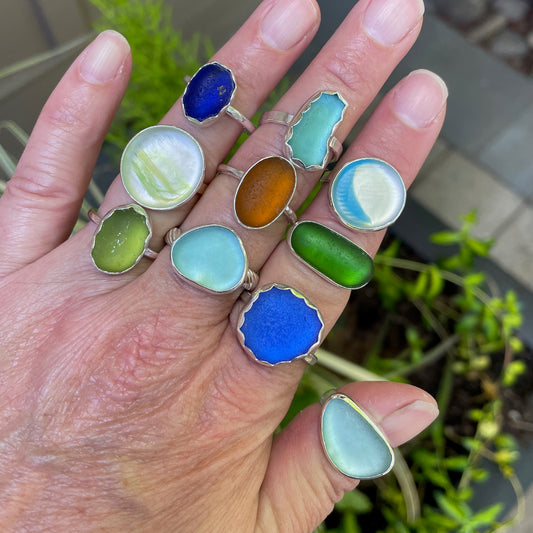 A large grouping of sea glass rings modeled on a hand. Handmade by Barb Macy of Accent Yourself in Corvallis, OR. 