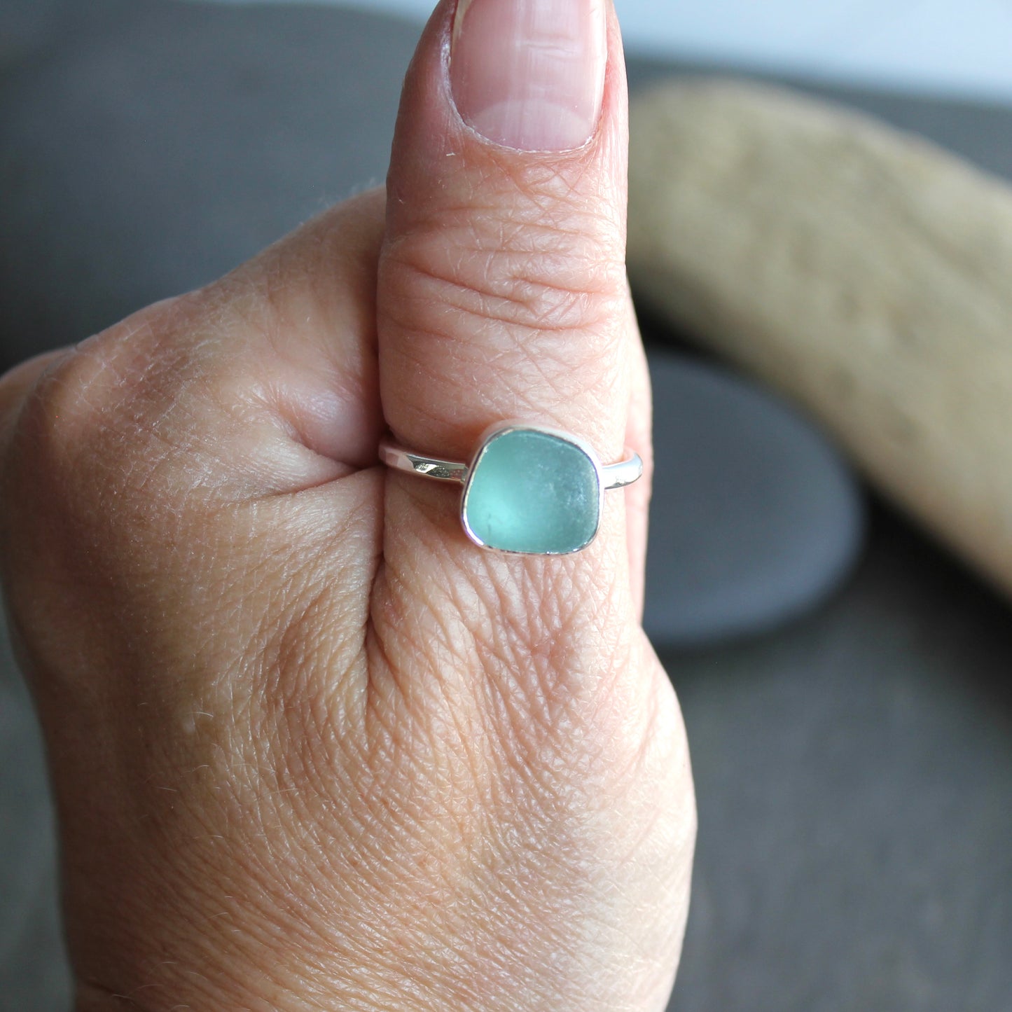 Hand wearing a ring with a light blue gemstone on a neutral background