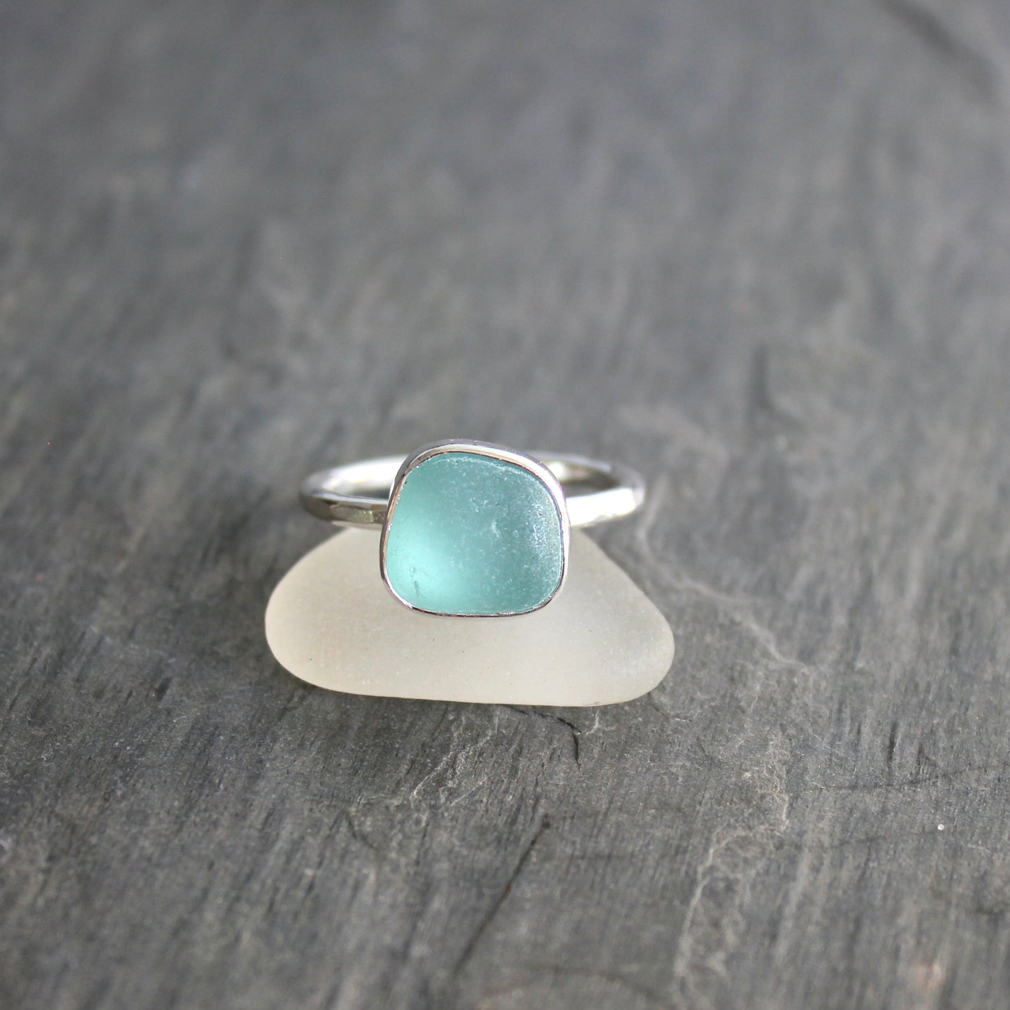 Silver ring with a turquoise stone on a piece of sea glass against a gray background