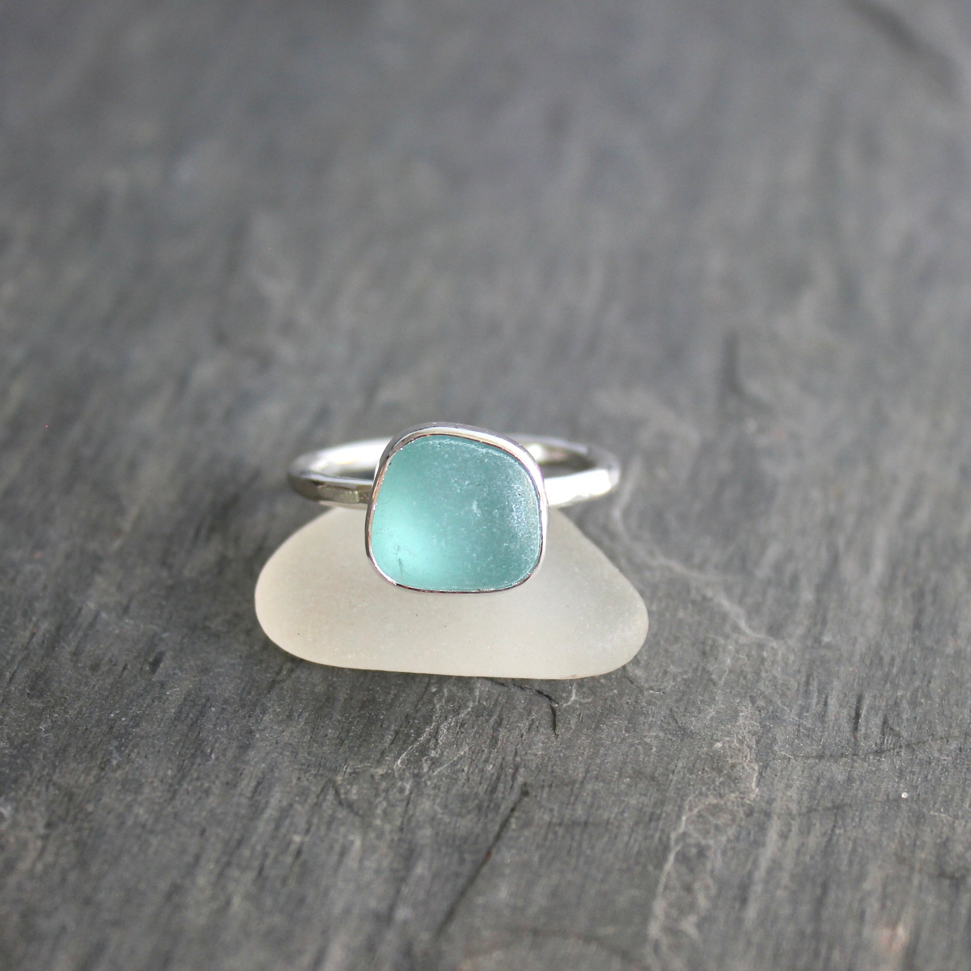 Silver ring with a turquoise stone on a piece of sea glass against a gray background