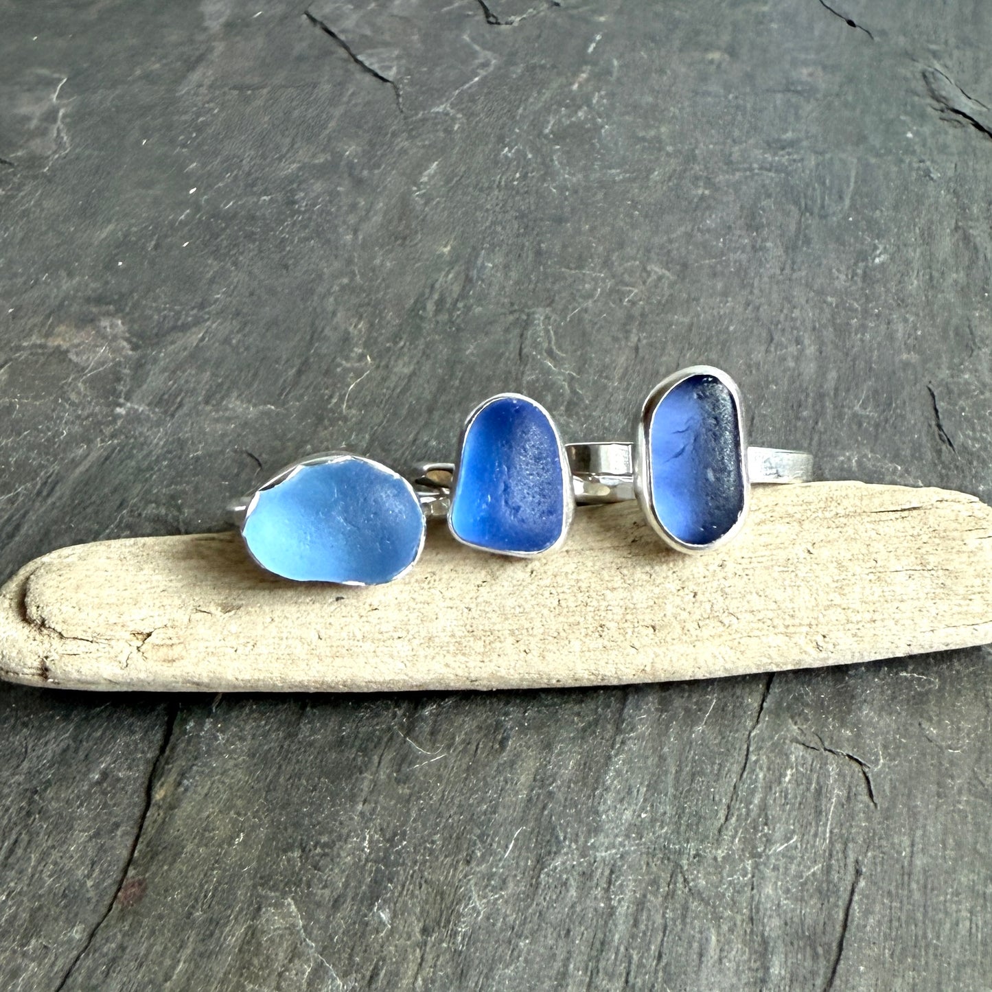 Three blue sea glass rings on a piece of driftwood with a dark gray background