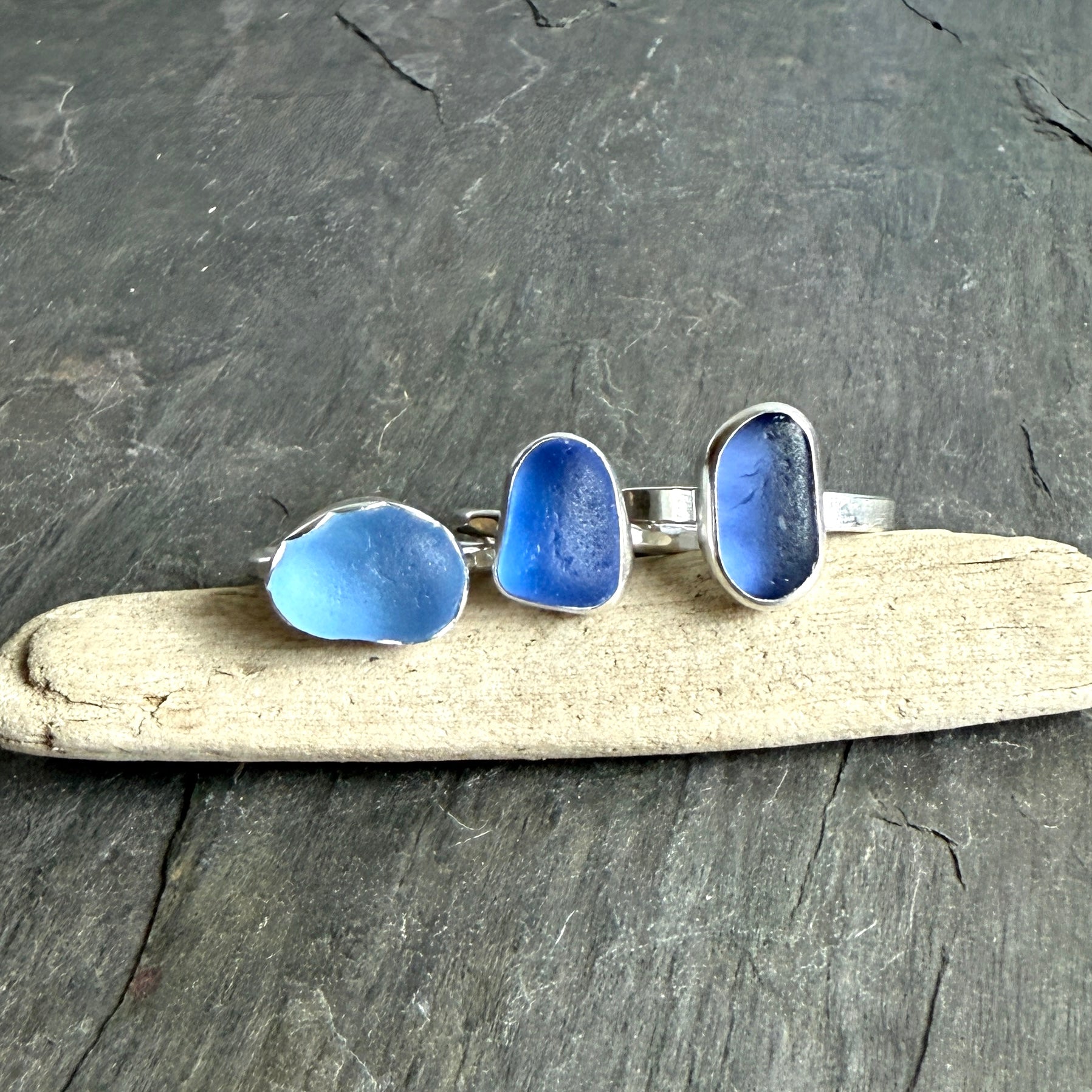 Three blue sea glass rings on a piece of driftwood with a dark gray background