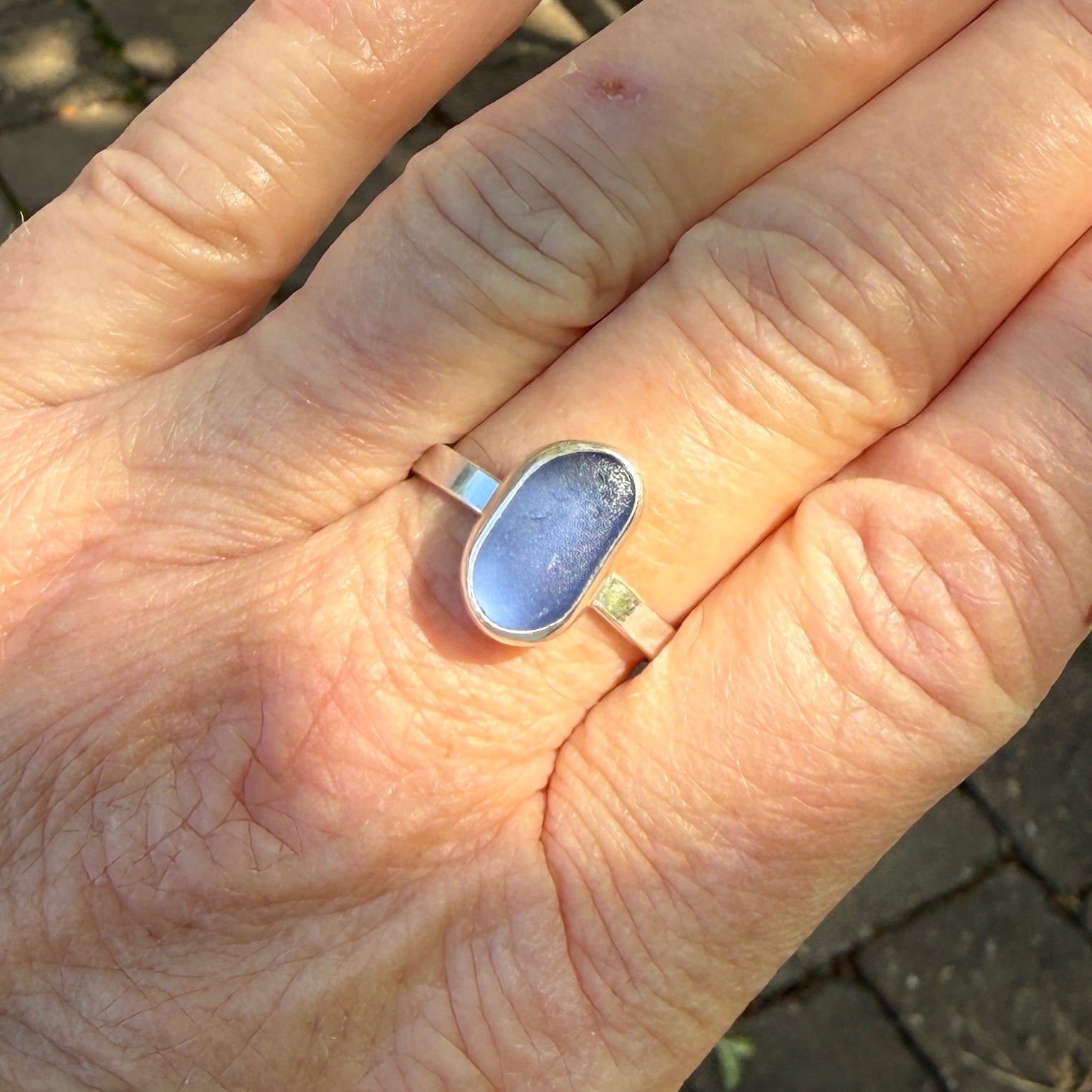 Hand wearing a blue ring with a silver band on a blurred background