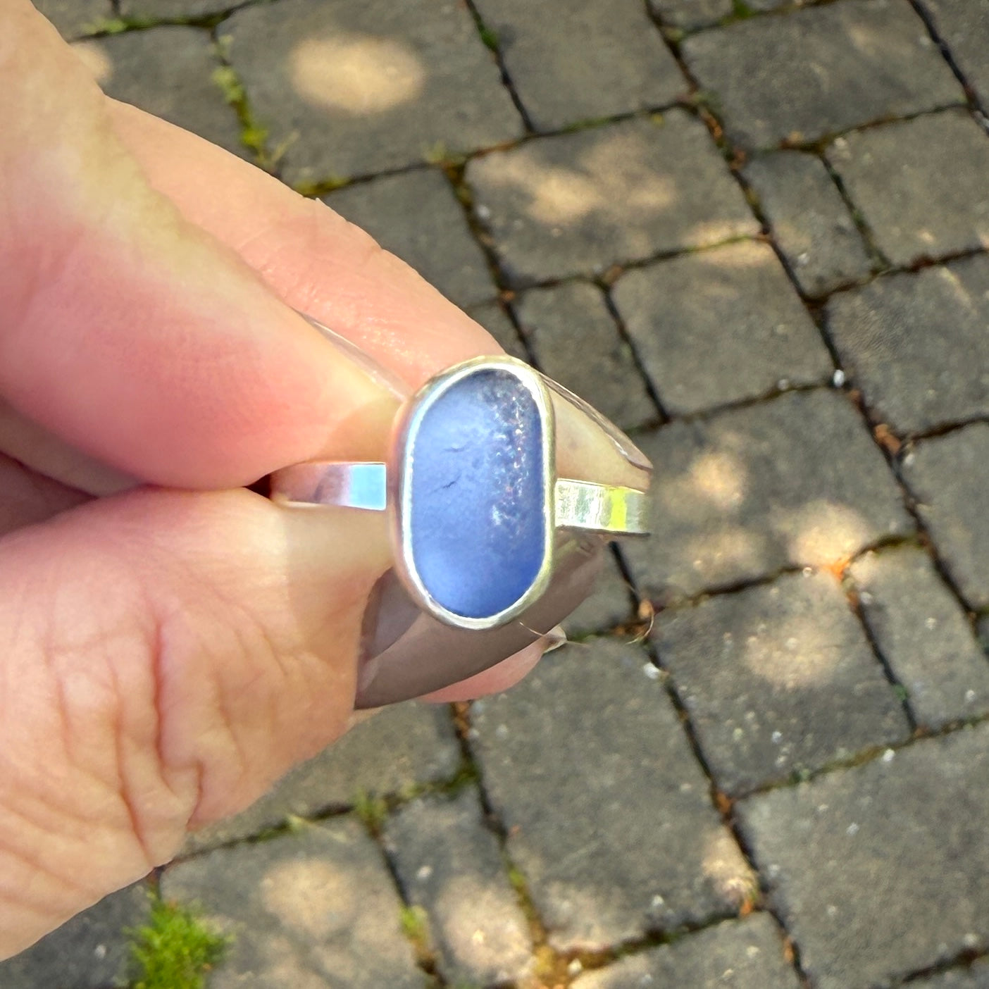 Hand wearing a blue ring on a paved surface