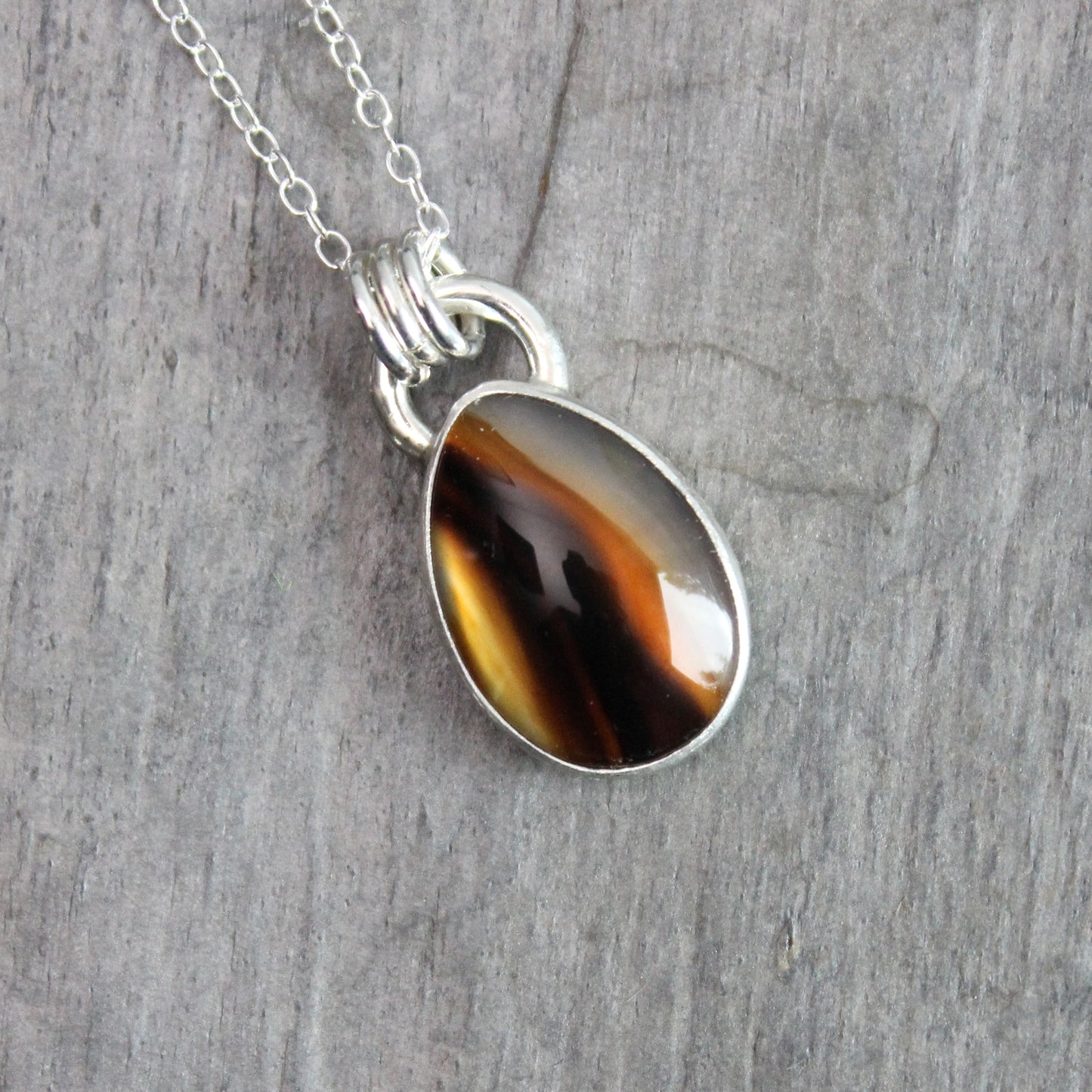 Montana Agate cabochon showing natural banded patterns and inclusions, set in sterling silver pendant