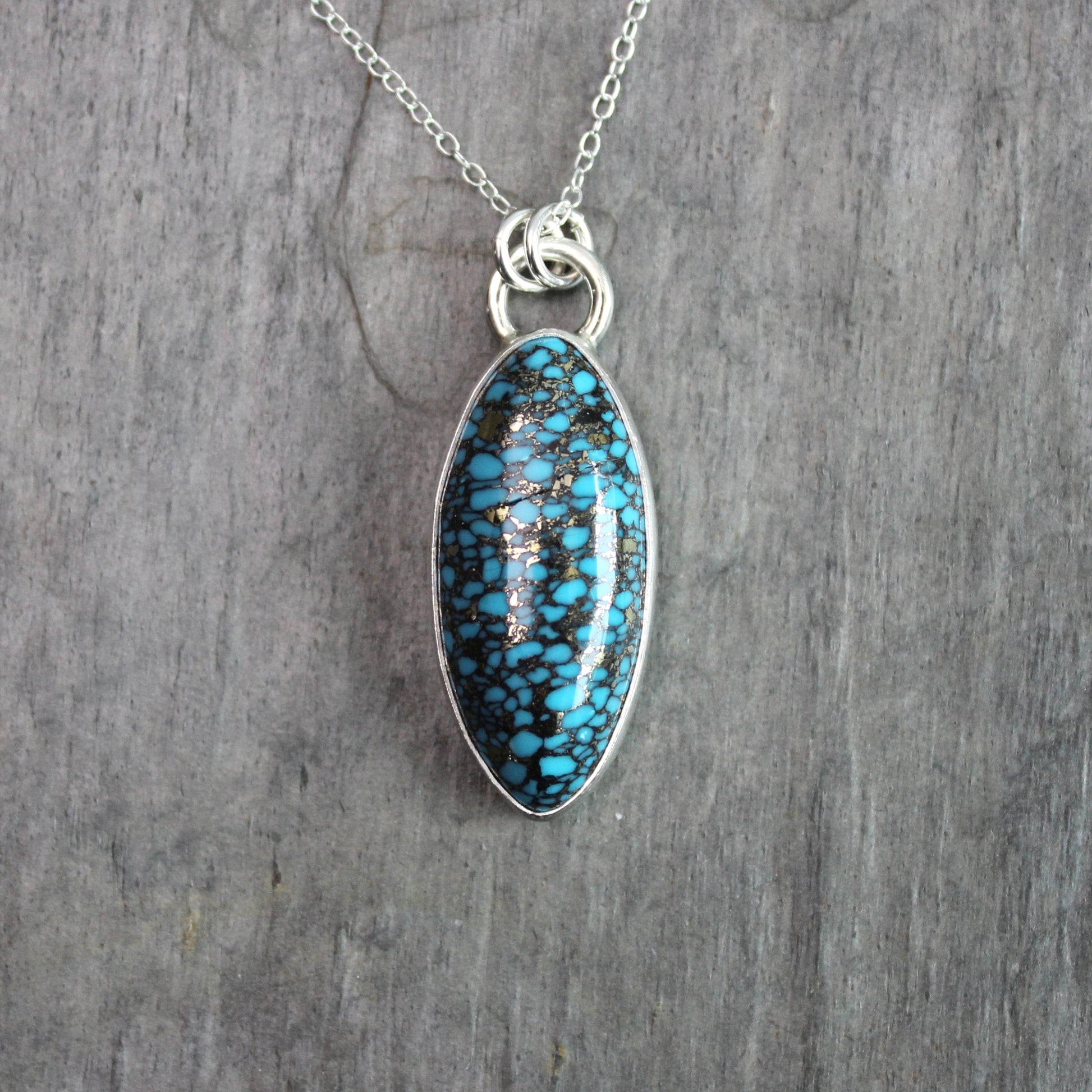 val spider web turquoise with pyrite pendant set in sterling silver with an adjustable silver chain, displayed on a rustic gray slate background.