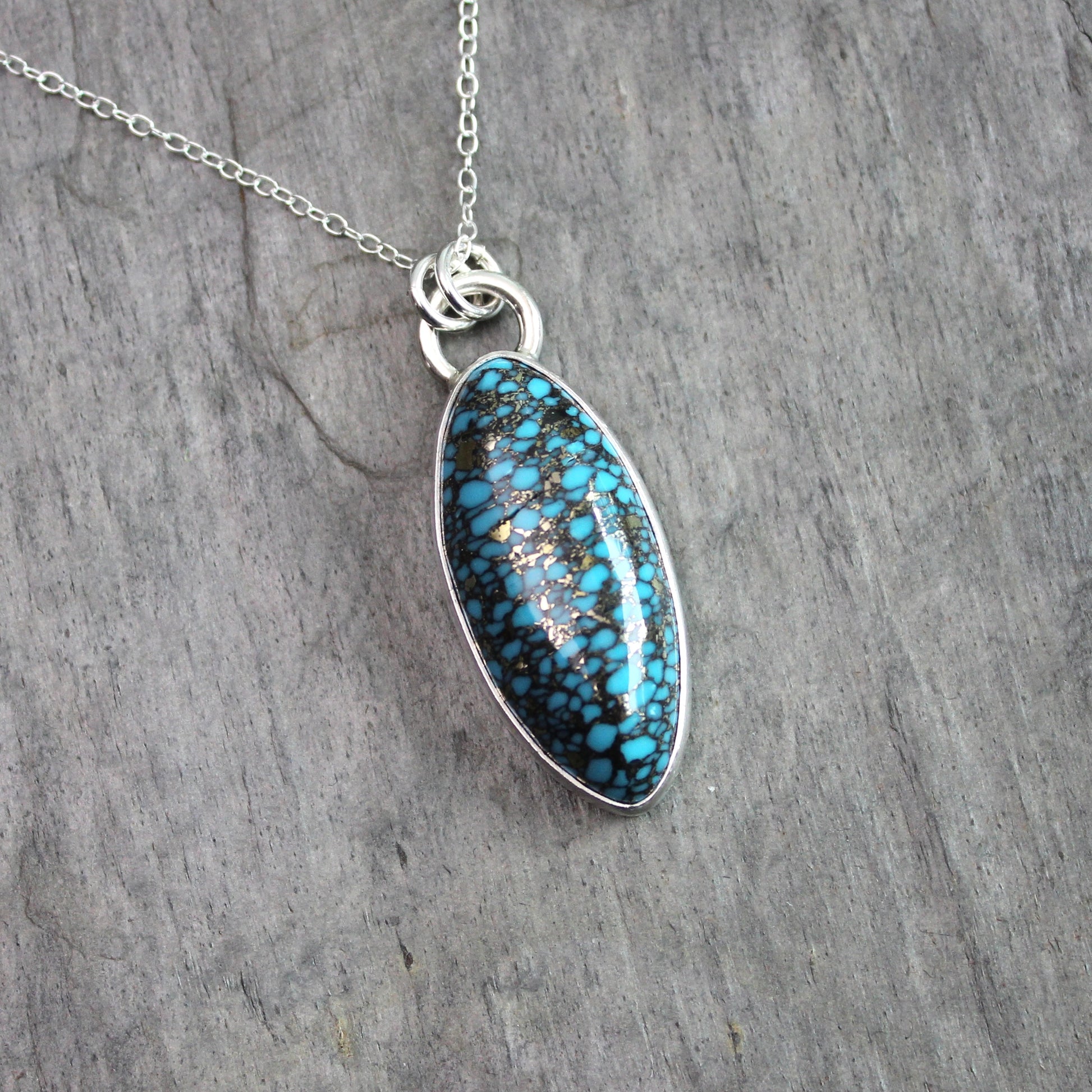 val spider web turquoise with pyrite pendant set in sterling silver with an adjustable silver chain, displayed on a rustic gray slate background.
