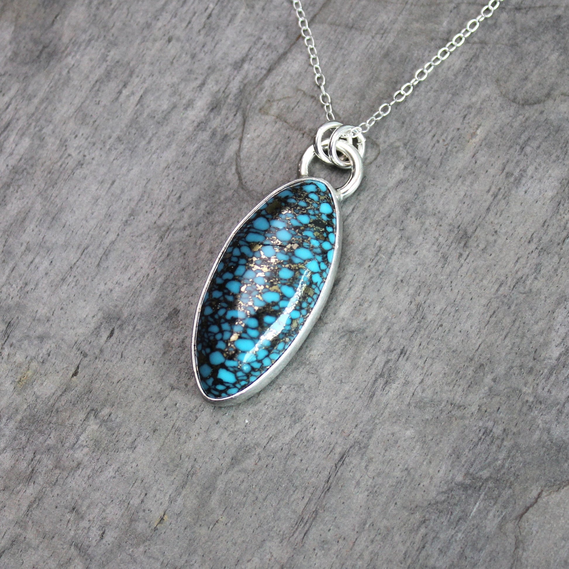 val spider web turquoise with pyrite pendant set in sterling silver with an adjustable silver chain, displayed on a rustic gray slate background.