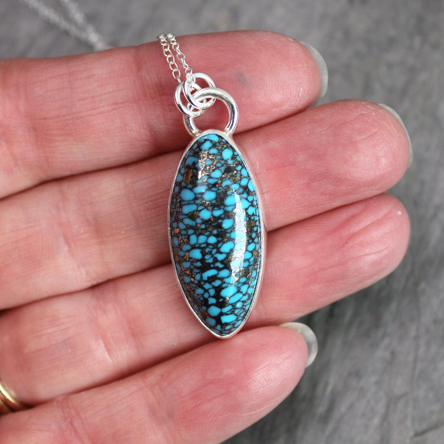 val spider web turquoise with pyrite pendant set in sterling silver with an adjustable silver chain, displayed in a hand.