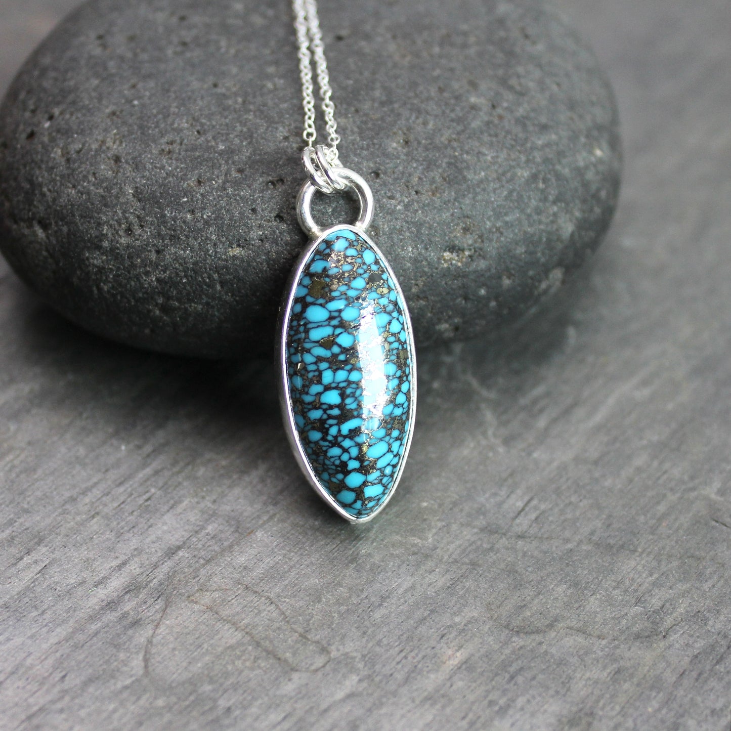 Oval spider web turquoise with pyrite pendant set in sterling silver with an adjustable silver chain, displayed on a rustic gray slate background.