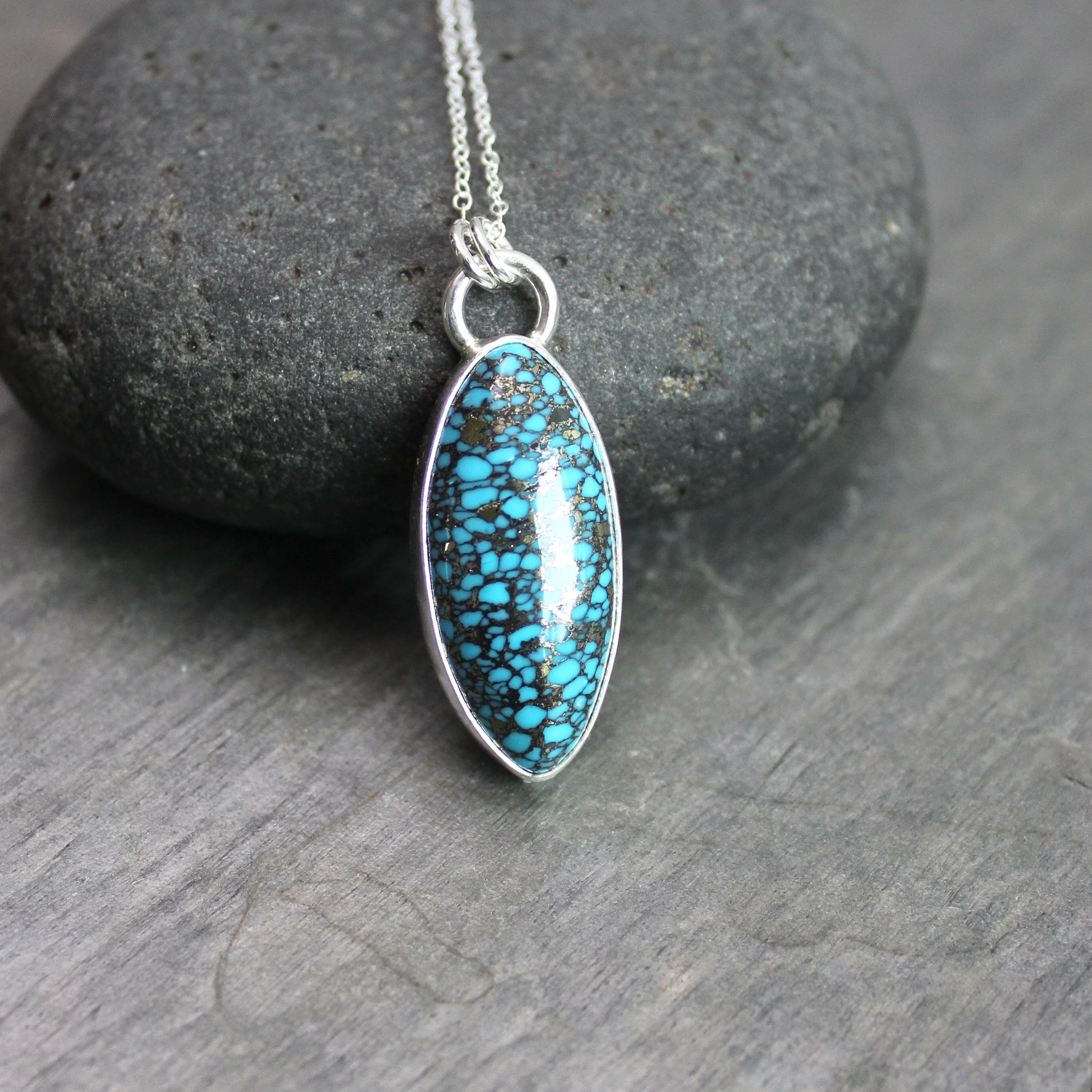 Oval spider web turquoise with pyrite pendant set in sterling silver with an adjustable silver chain, displayed on a rustic gray slate background.
