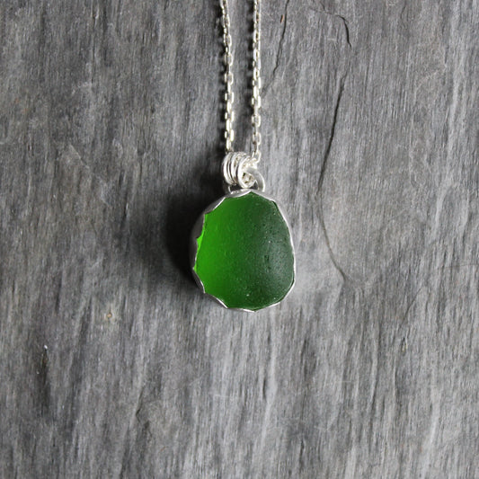 This pendant necklace has a bright green UV piece of sea glass that is set in a fine and sterling silver scalloped bezel on a sturdy silver chain. The uranium sea glass glows under a black light. Handmade by Barb Macy in Corvallis, OR