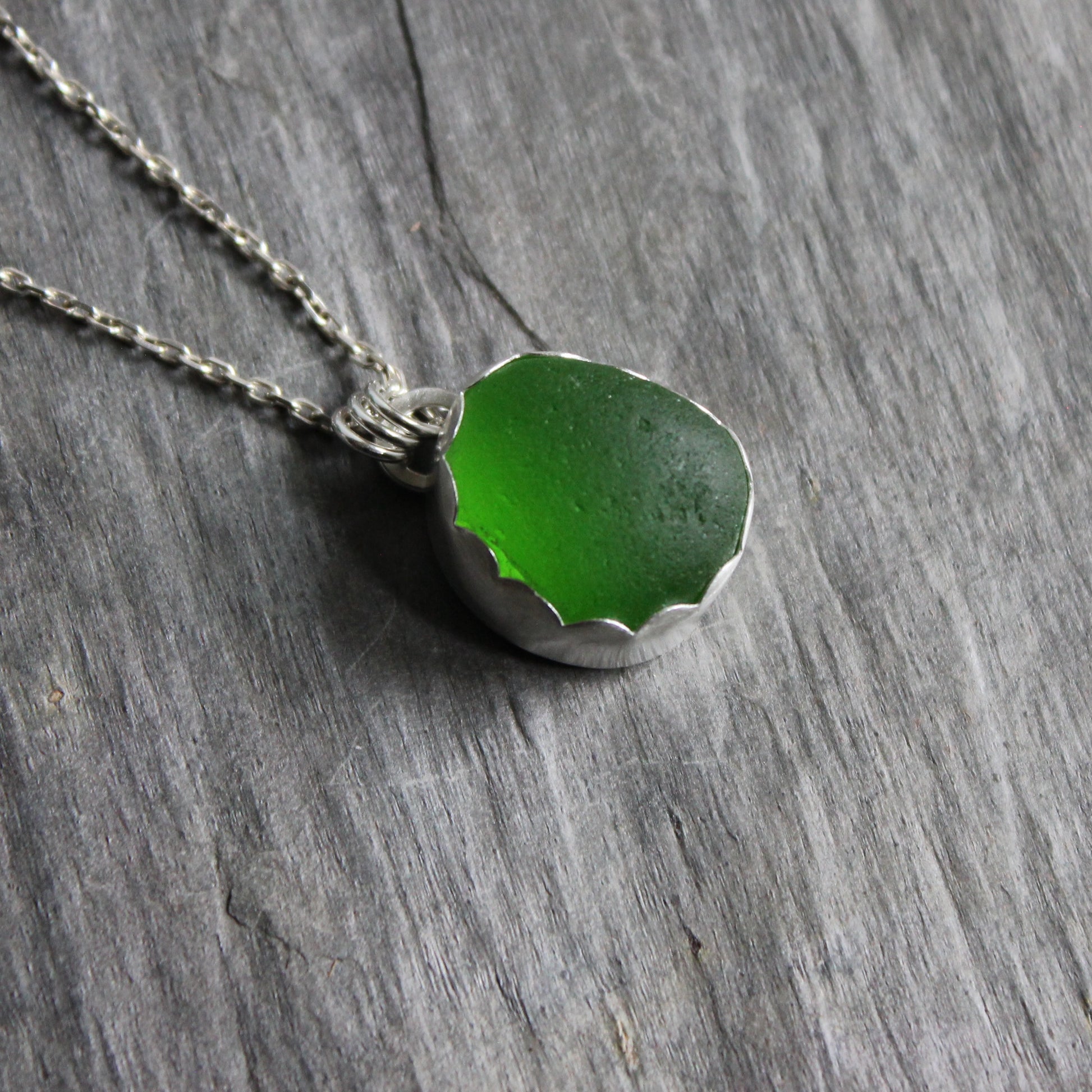 This pendant necklace has a bright green UV piece of sea glass that is set in a fine and sterling silver scalloped bezel on a sturdy silver chain. The uranium sea glass glows under a black light. Handmade by Barb Macy in Corvallis, OR
