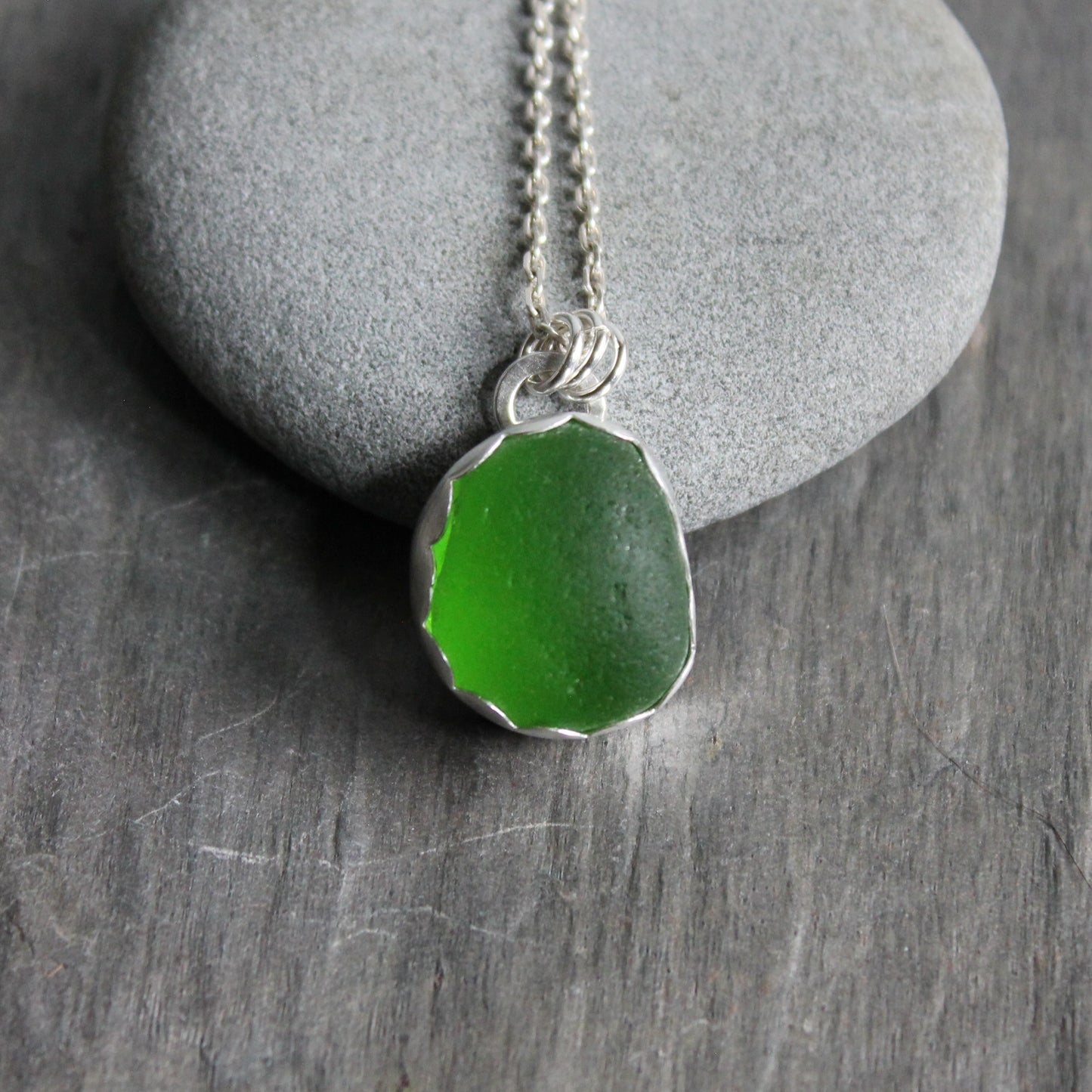 This pendant necklace has a bright green UV piece of sea glass that is set in a fine and sterling silver scalloped bezel on a sturdy silver chain. The uranium sea glass glows under a black light. Handmade by Barb Macy in Corvallis, OR