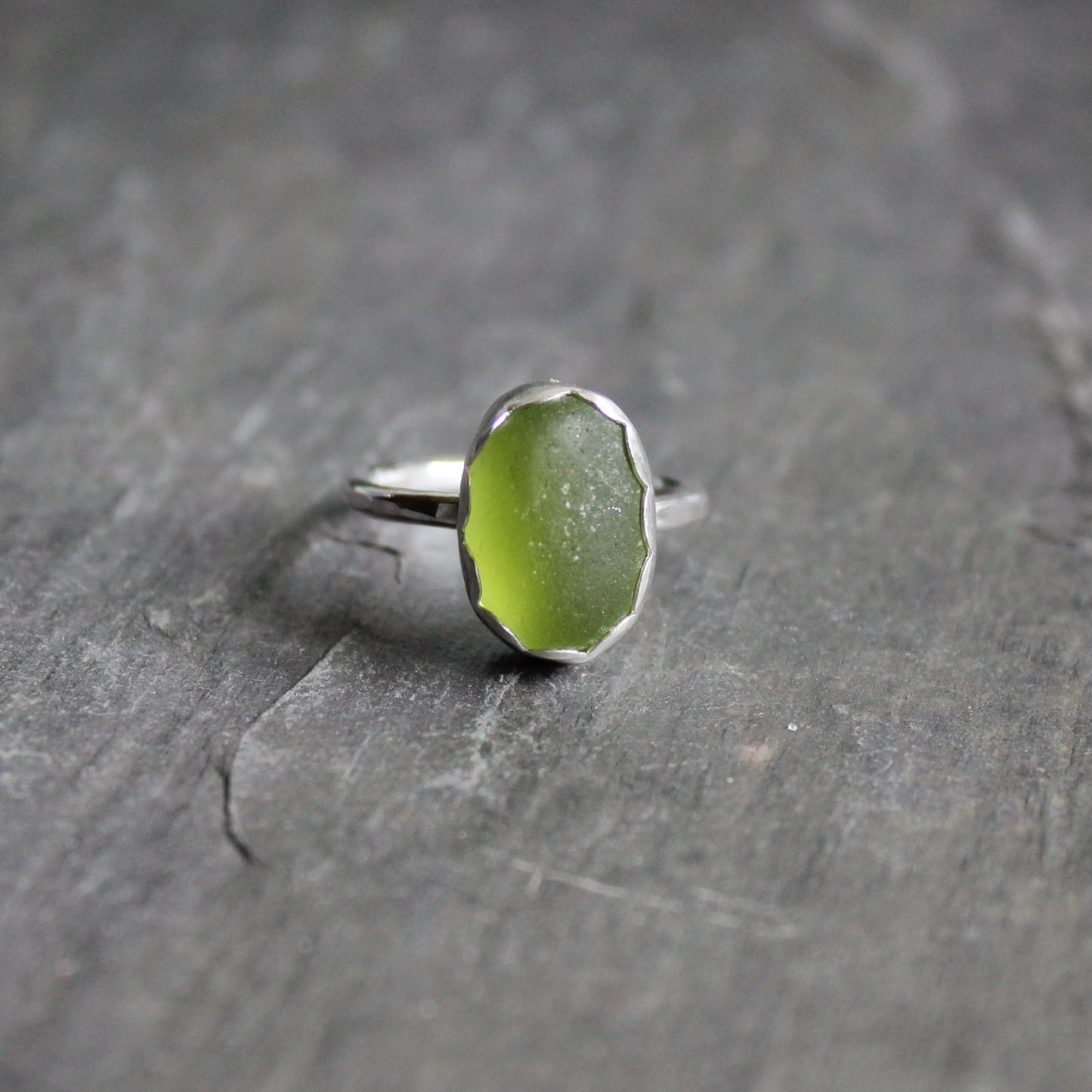This ring has a piece of olive green sea glass set in a fine and sterling silver scalloped bezel on a sturdy silver band.  Size 7 3/4