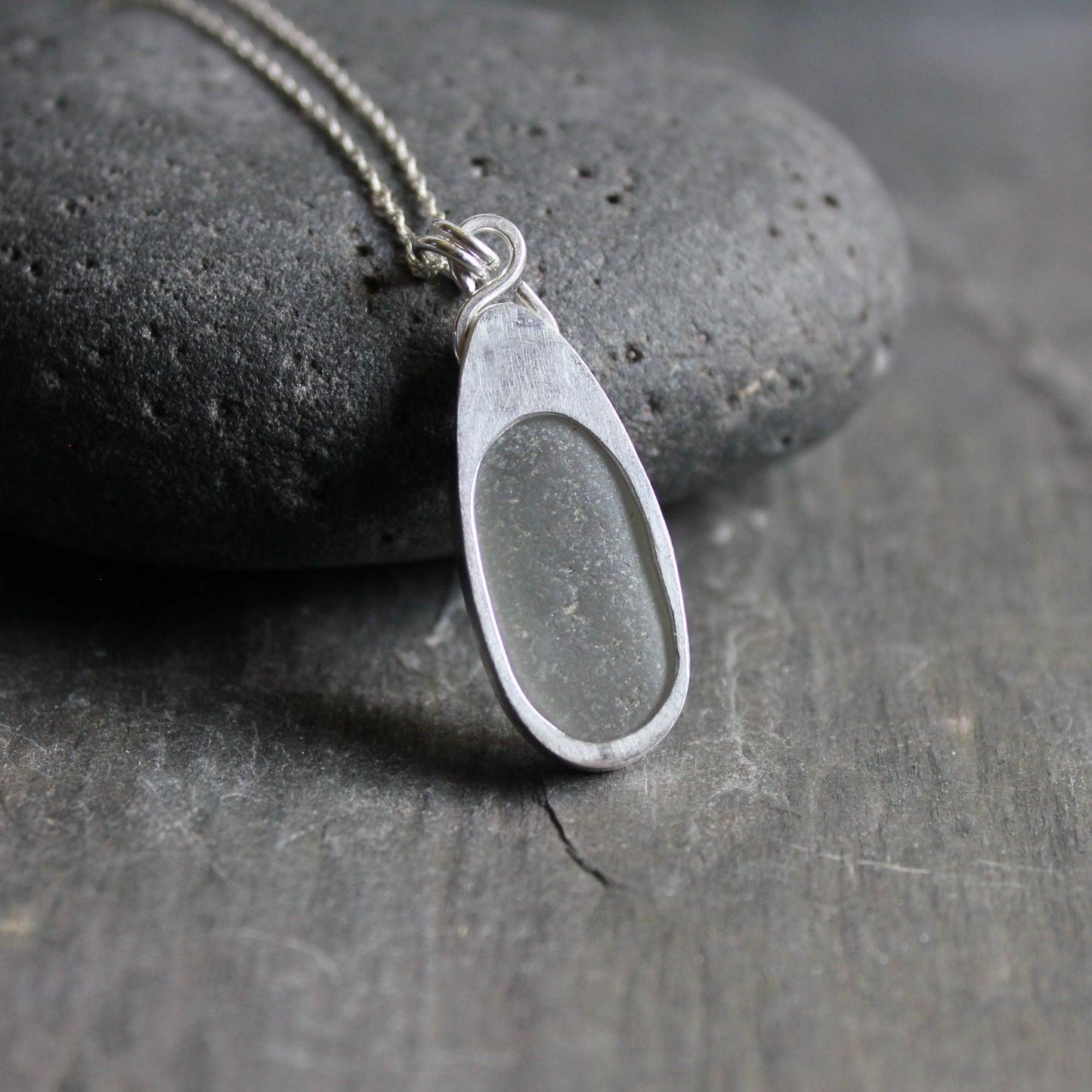 This necklace has a large piece of gray sea glass that is set in a bezel with a simple bail and the back plate cut out so light can shine through the glass. It has a 4mm cubic zirconia to add a little sparkle! It will arrive to you on a sterling silver chain that can be worn at 16, 18 or 20 inches.. All of our sea glass is found and not altered in any way. Handmade by Barb Macy in Corvallis, Oregon. 
