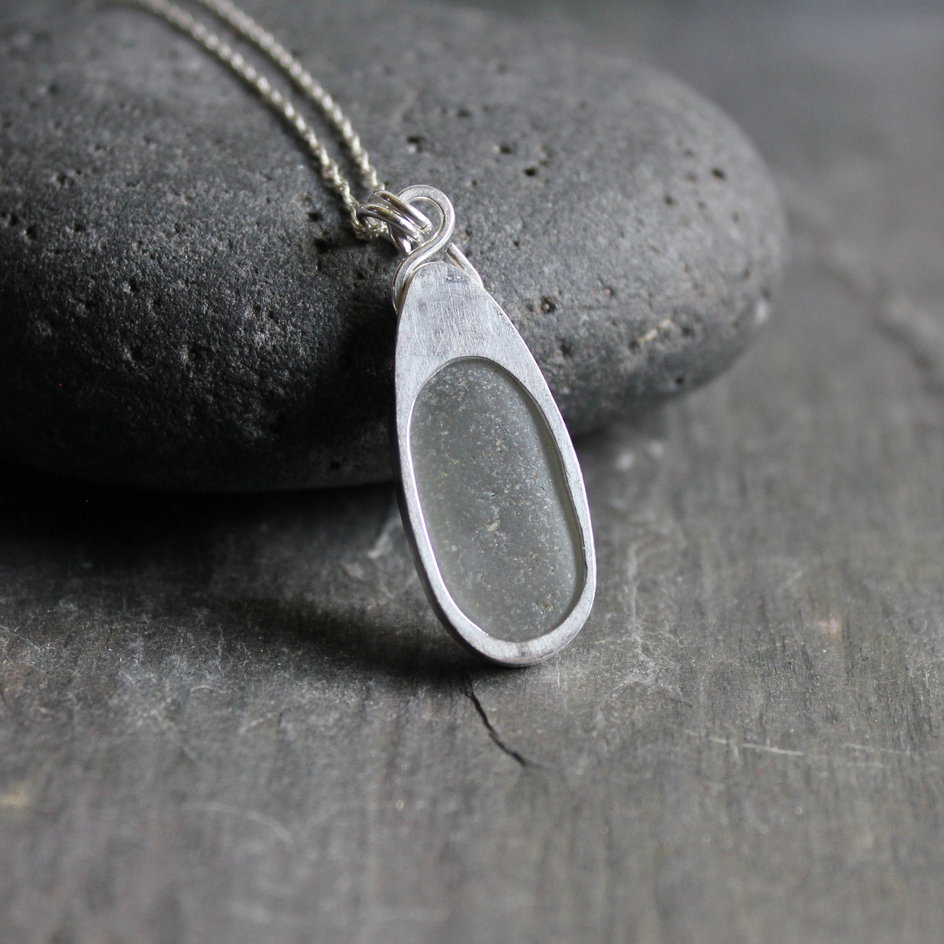 This necklace has a large piece of gray sea glass that is set in a bezel with a simple bail and the back plate cut out so light can shine through the glass. It has a 4mm cubic zirconia to add a little sparkle! It will arrive to you on a sterling silver chain that can be worn at 16, 18 or 20 inches.. All of our sea glass is found and not altered in any way. Handmade by Barb Macy in Corvallis, Oregon. 
