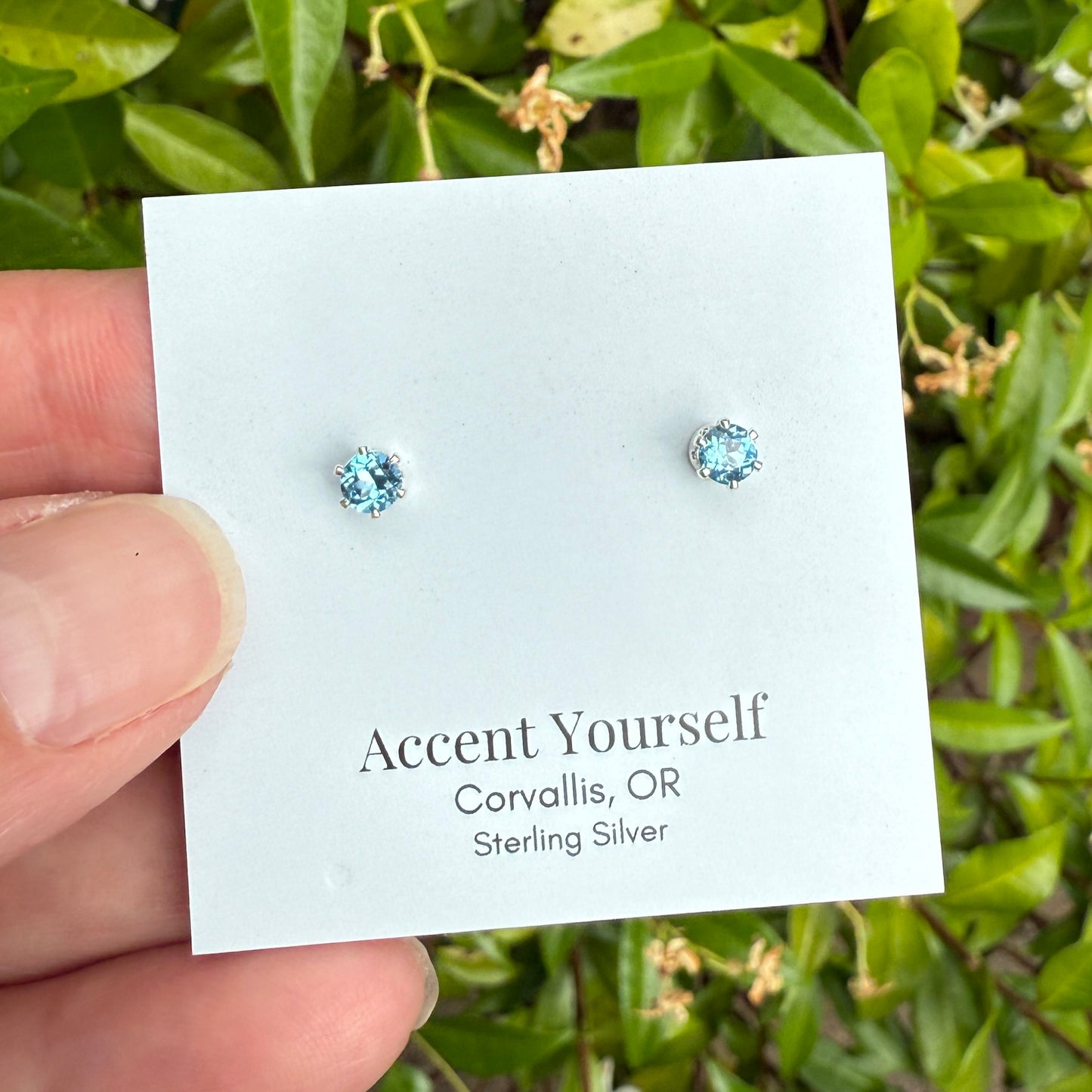 Pair of silver earrings on a 'Accent Yourself' card with green foliage in the background
