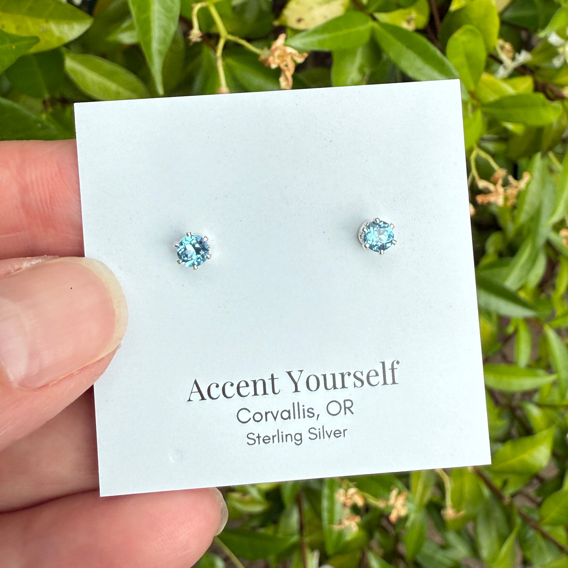 Pair of silver earrings on a 'Accent Yourself' card with green foliage in the background
