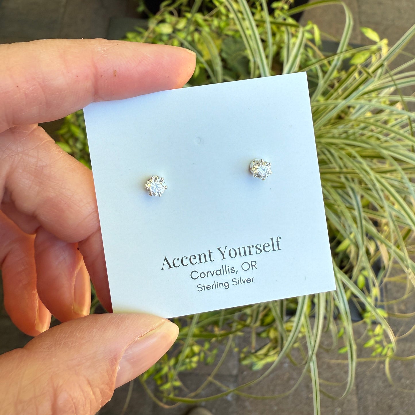 Hand holding a card with silver earrings on a natural background