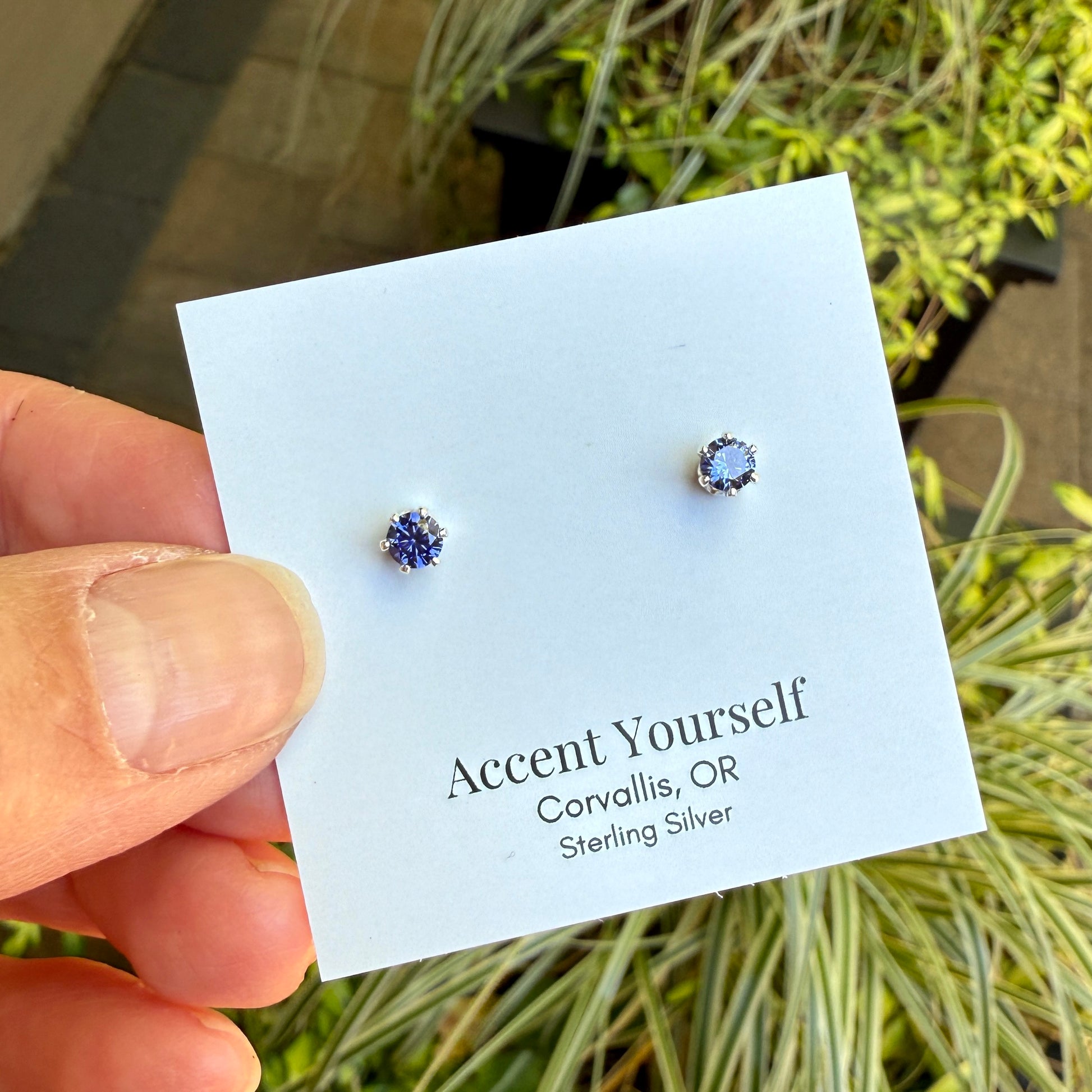 Pair of silver earrings on a 'Accent Yourself' card held by a hand with a natural background.