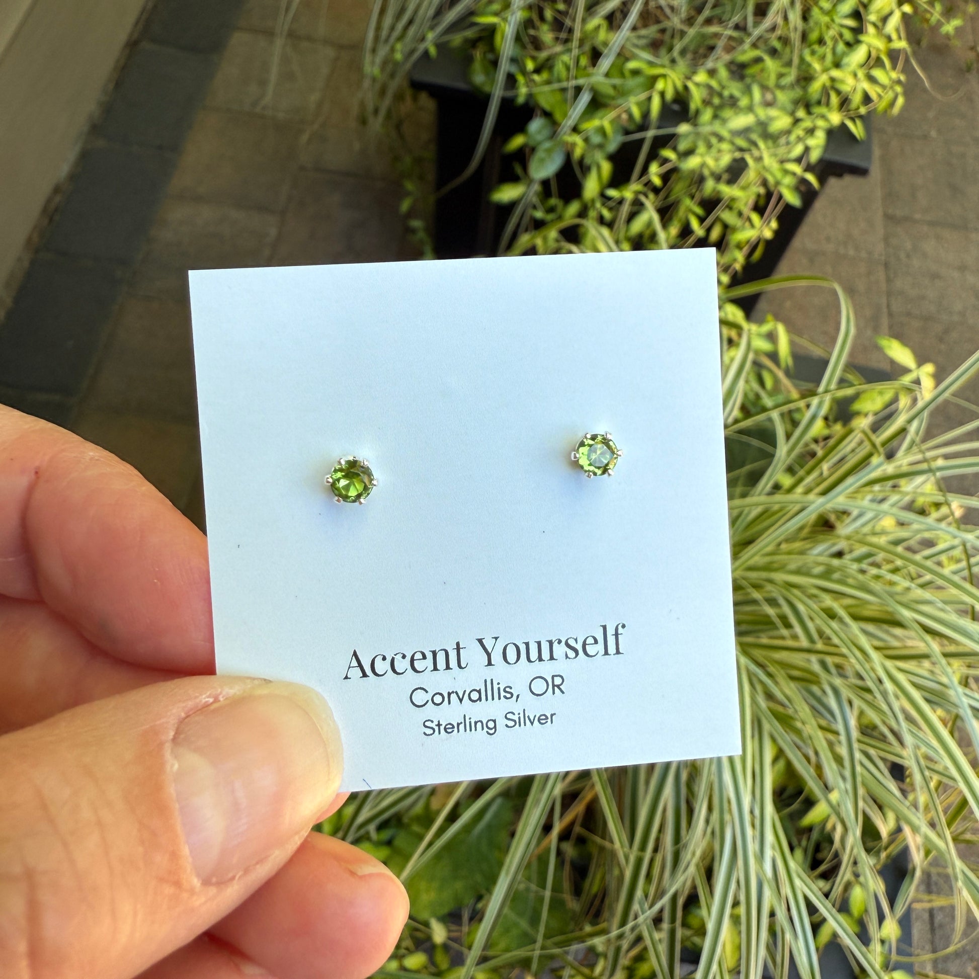 Green gemstone earrings on a 'Accent Yourself' card held in front of plants.