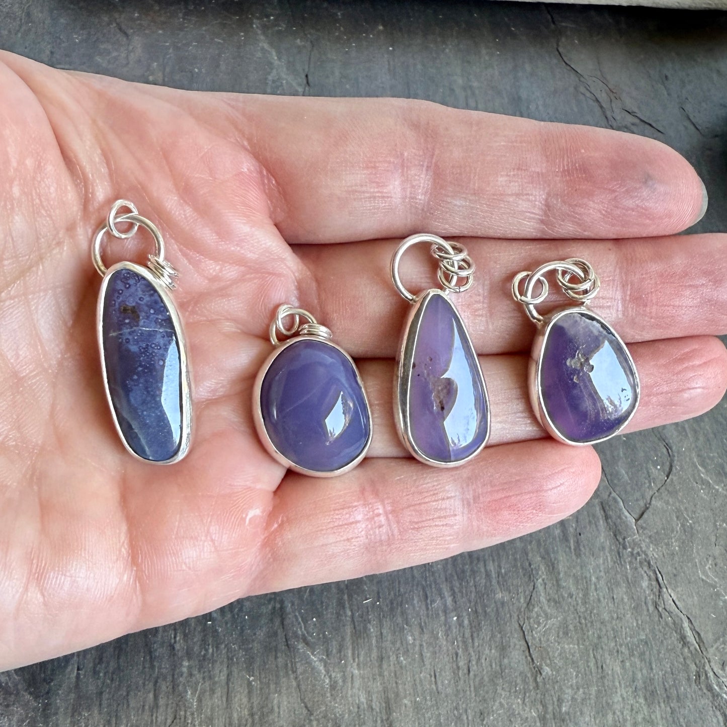 Four purple teardrop pendants with silver settings on a hand. A long holley blue agate cabochon set in a fine and sterling silver bezel setting on a sturdy silver chain. 