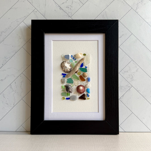 Framed artwork with sea glass and shells on a white background