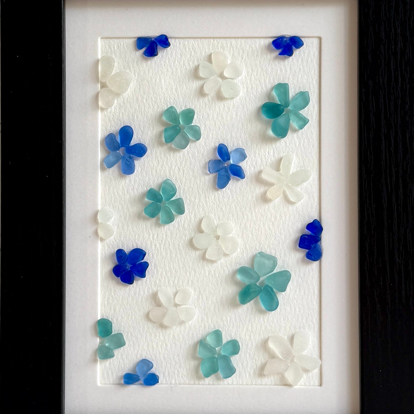 Decorative wall art with blue, green, and white flowers on a textured white background.