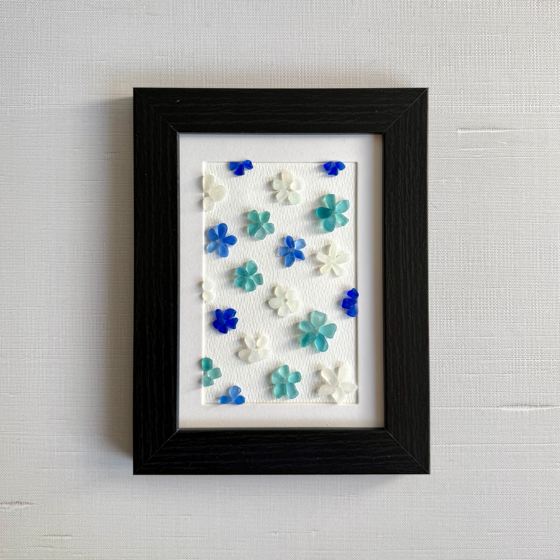 Framed artwork with colorful flower-shaped objects on a textured wall.