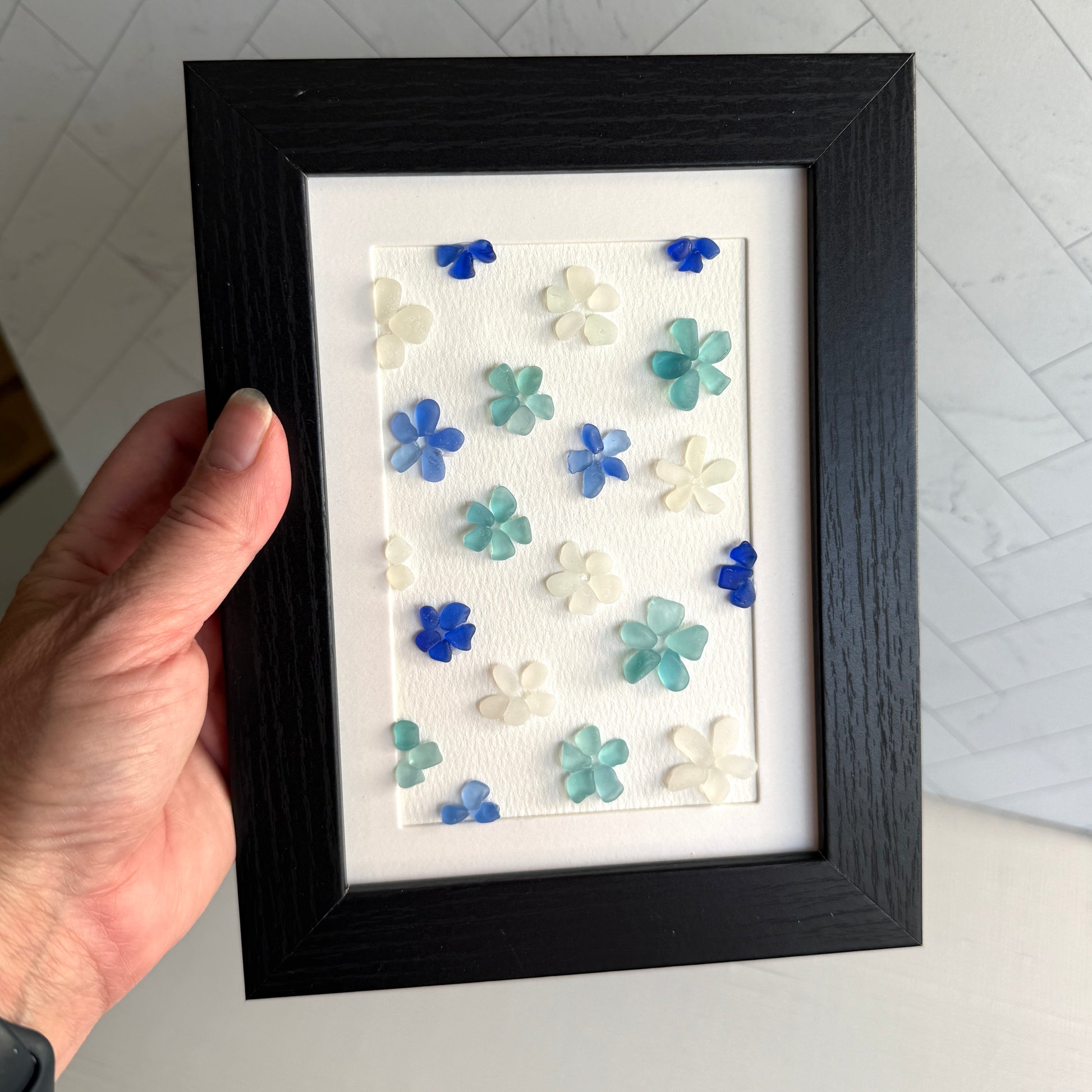 Framed artwork with blue and white floral patterns held by a hand.
