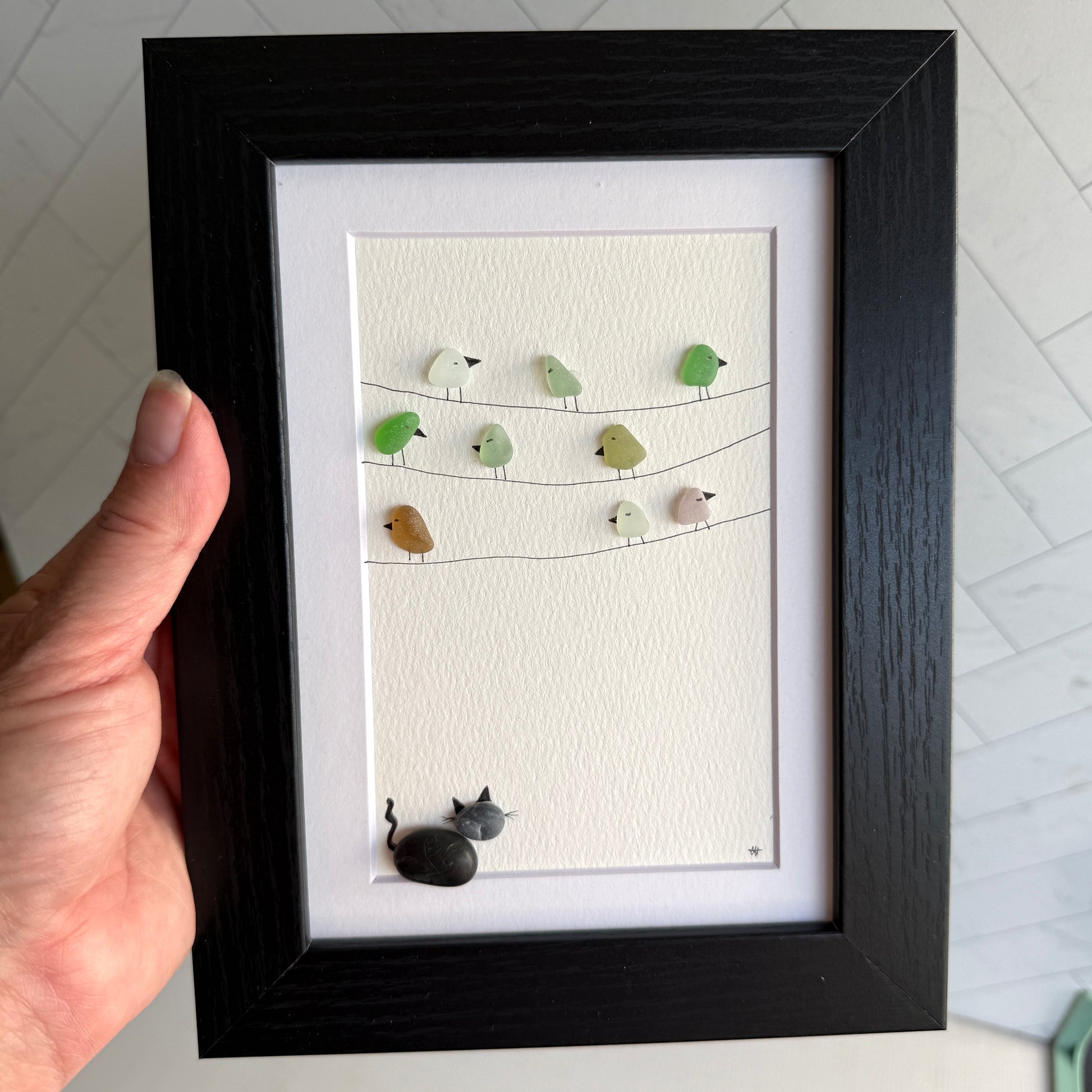 Framed sea glass artwork with birds and a pebble cat on a white background