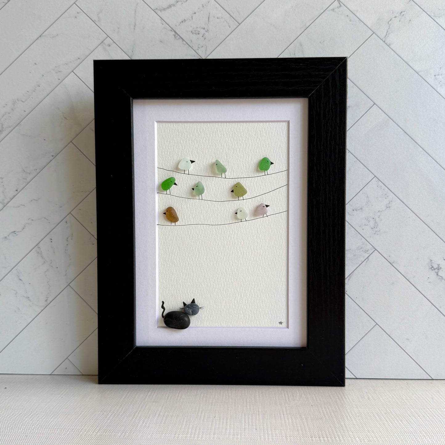 Framed sea glass artwork with birds and a pebble cat on a white background