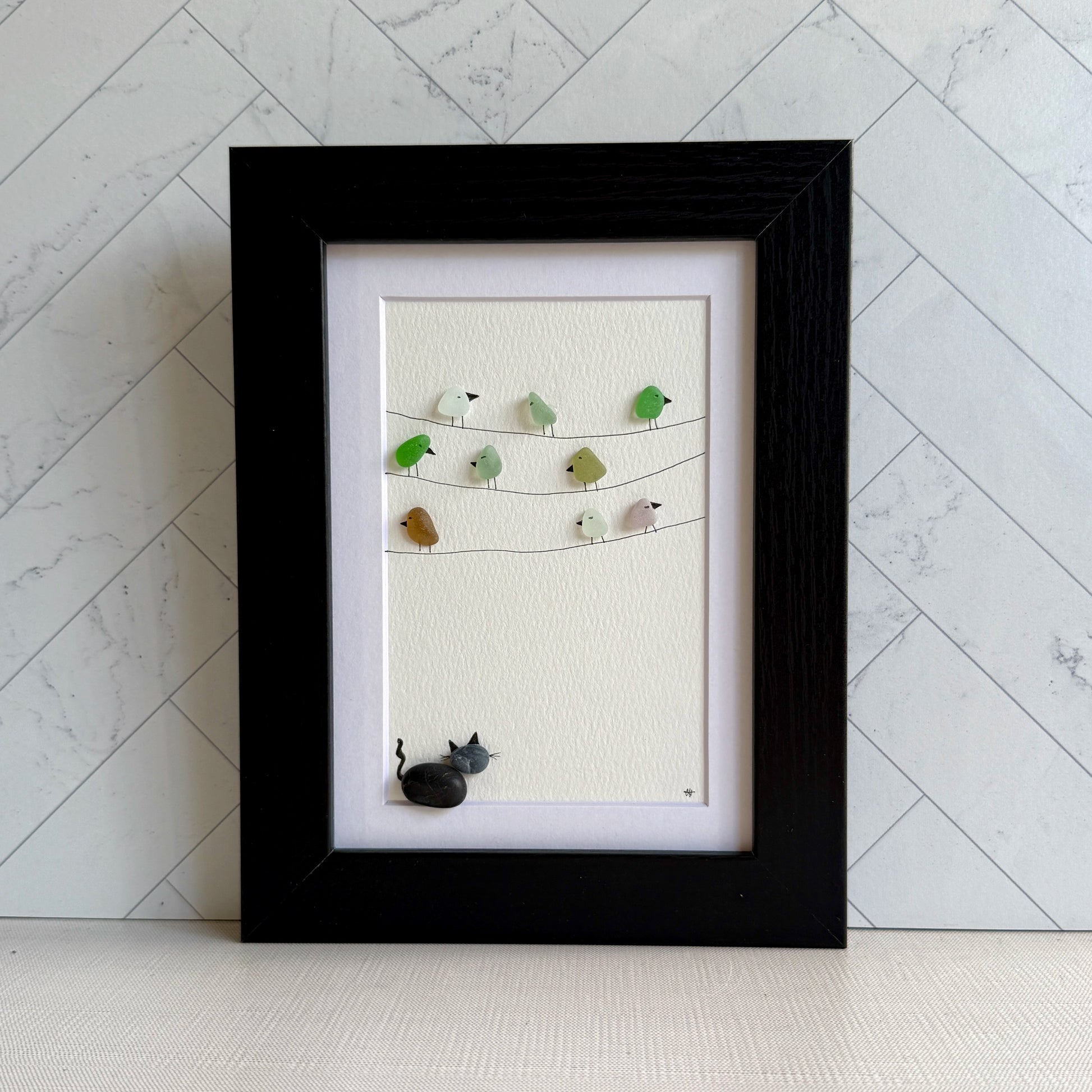 Framed sea glass artwork with birds and a pebble cat on a white background