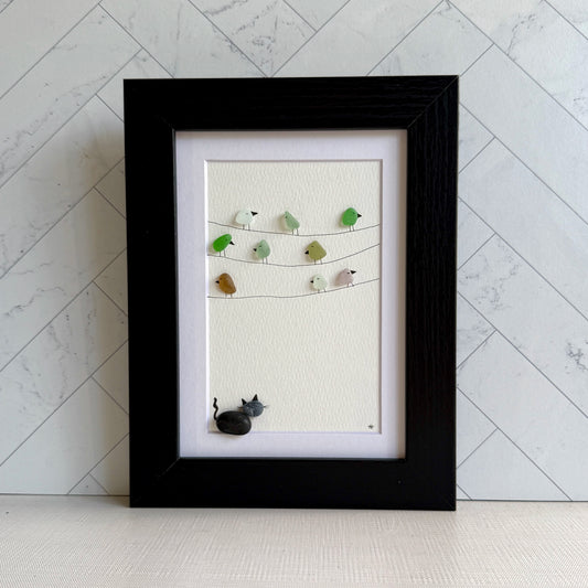 Framed sea glass artwork with birds and a pebble cat on a white background