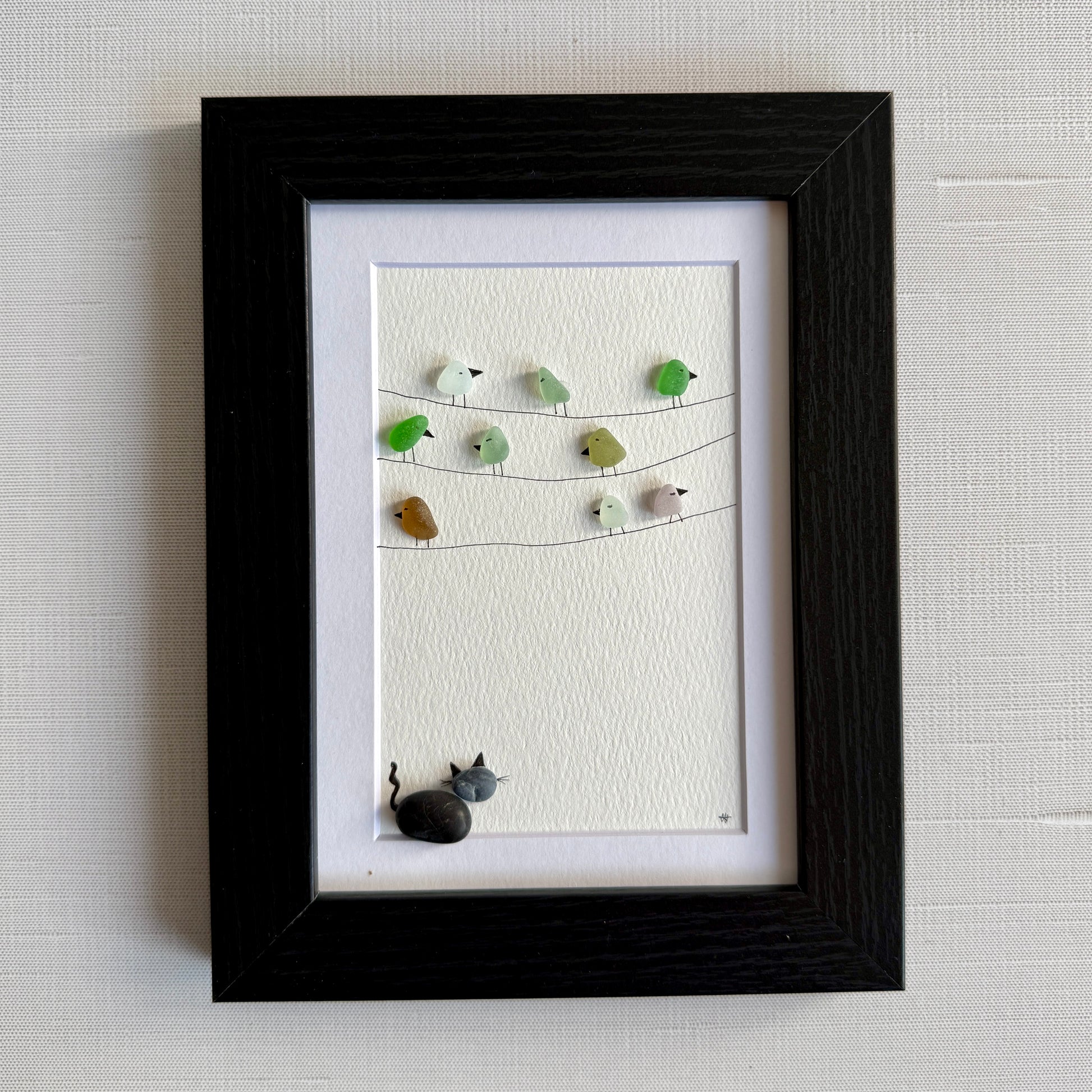 Framed sea glass artwork with birds and a pebble cat on a white background