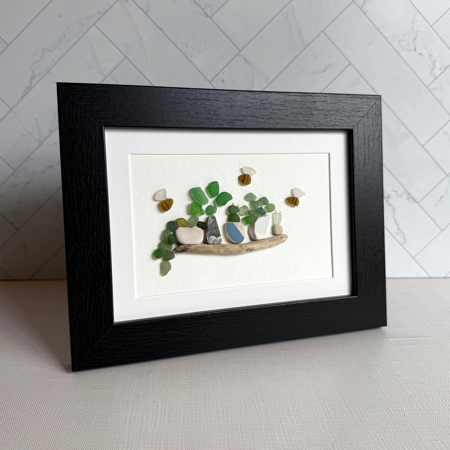 Framed artwork made of stones on a white surface with a marble wall background