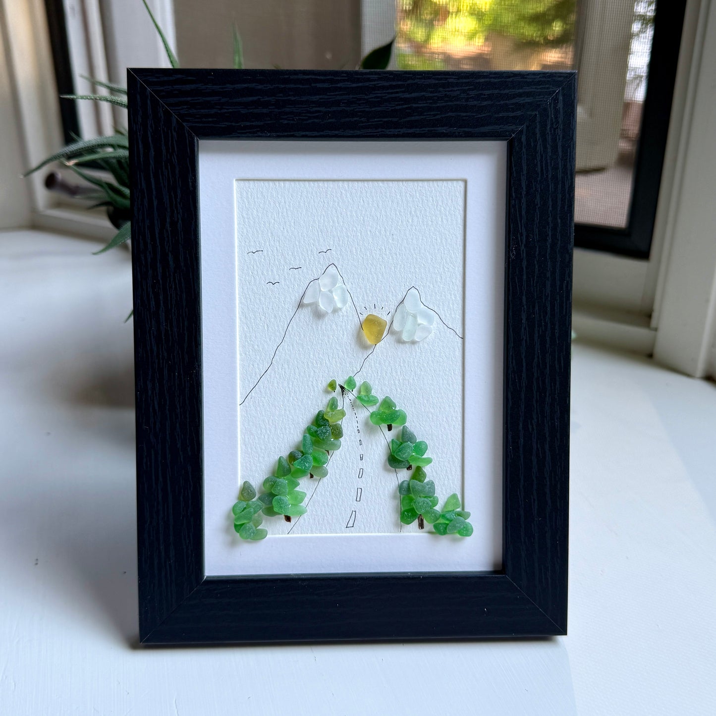 Framed artwork with green leaf-like elements on a white background