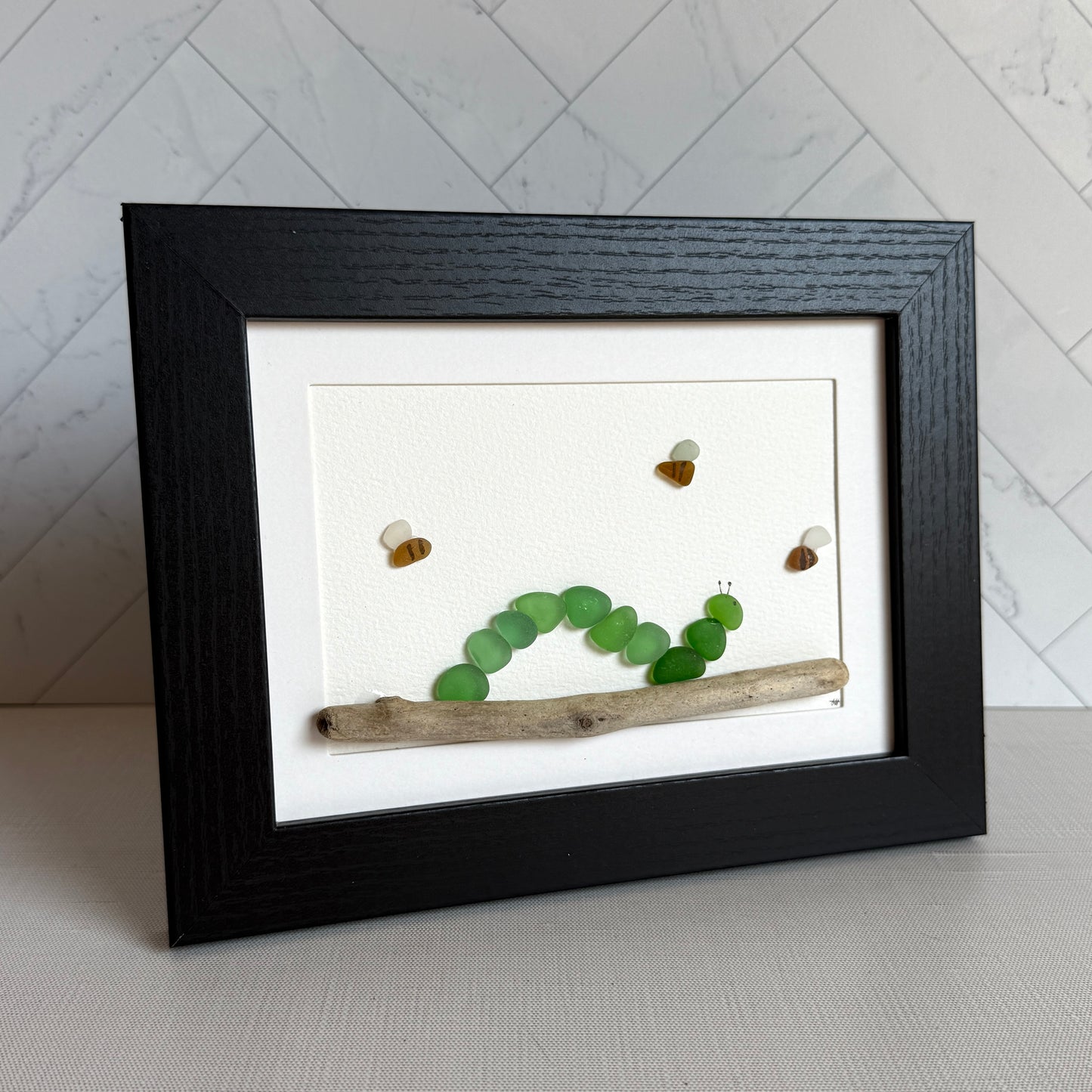 Framed artwork with green glass pieces and small objects on a white background