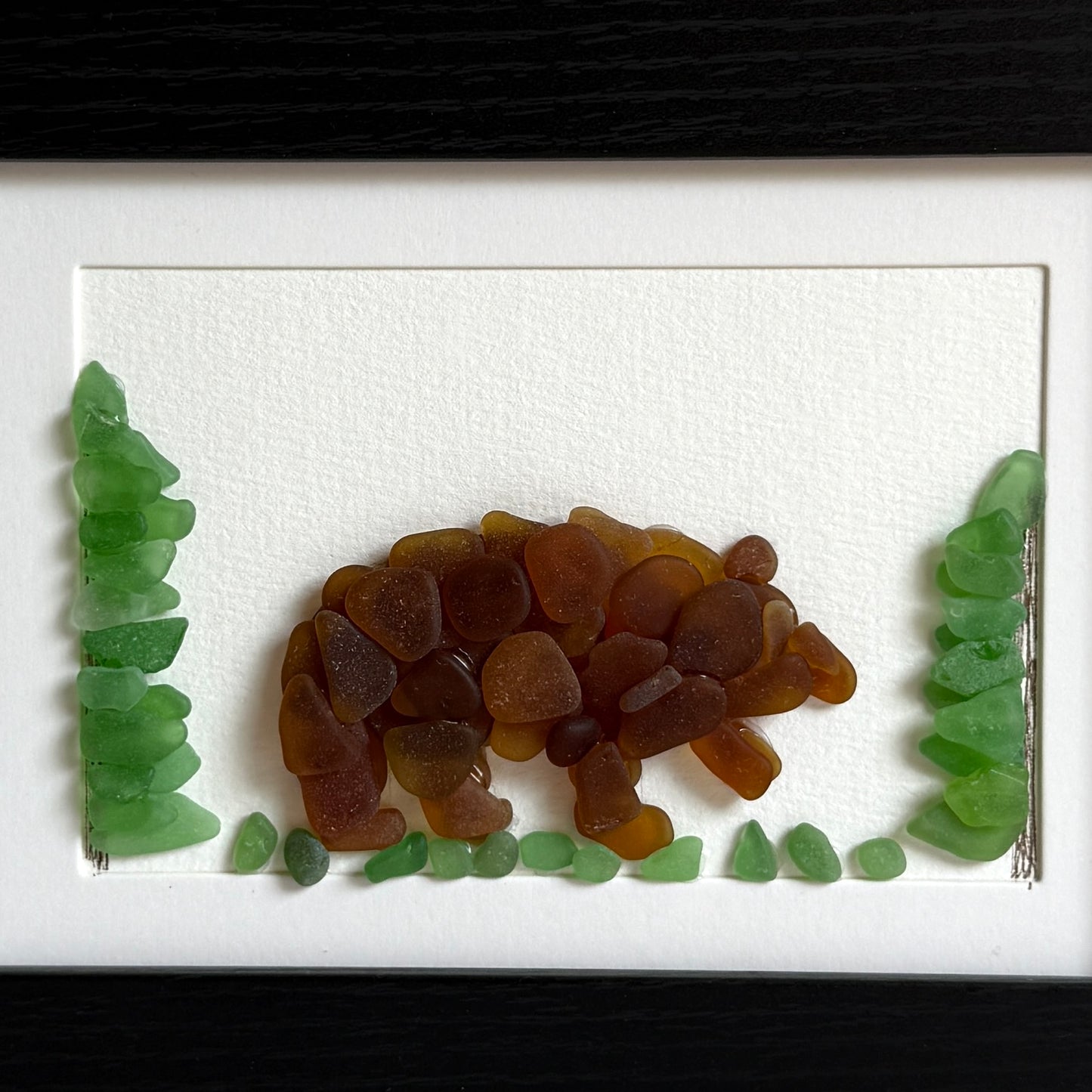 Artistic depiction of a bear made from brown and green glass pieces on a white background