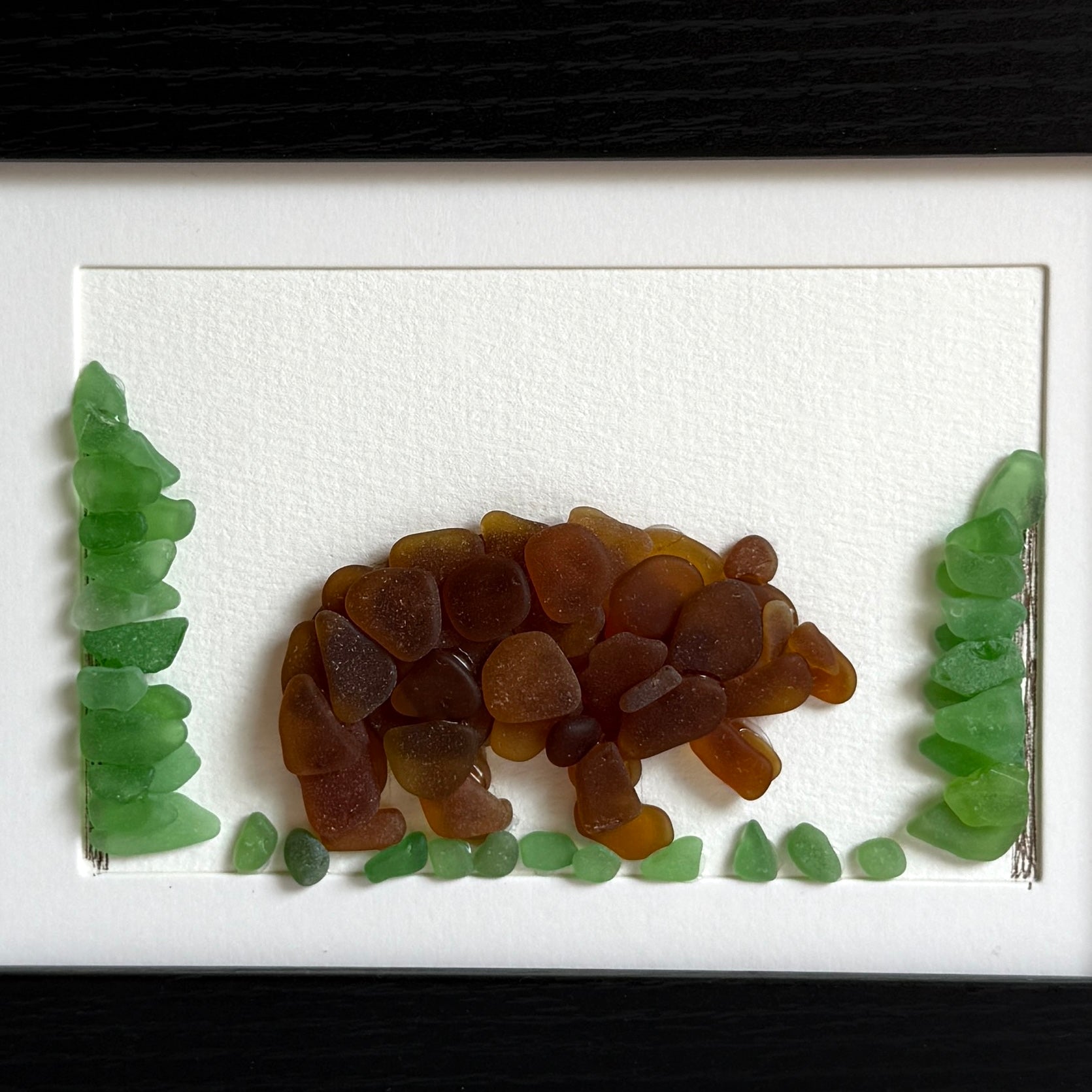 Artistic depiction of a bear made from brown and green glass pieces on a white background
