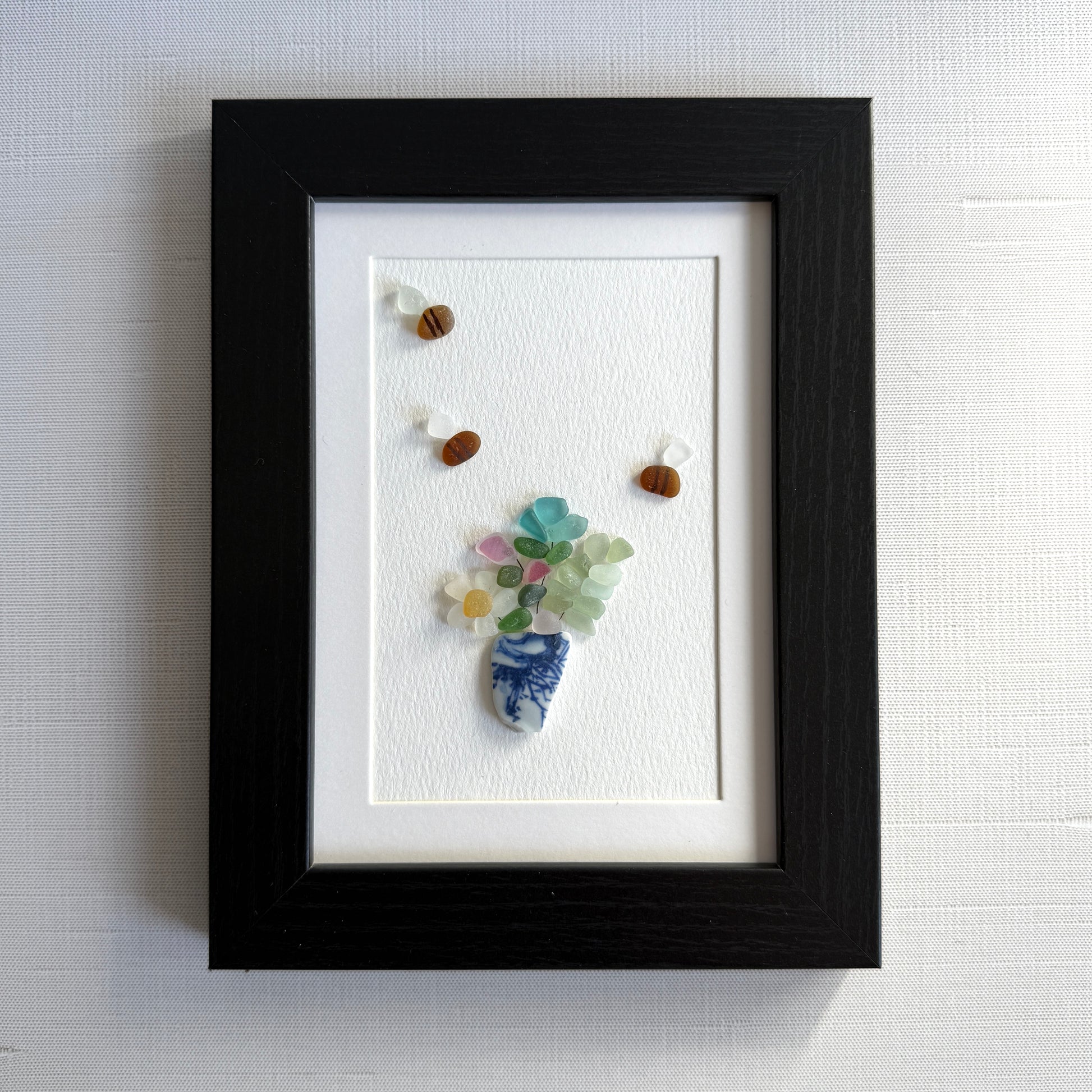 Framed artwork made from small stones and beads on a white background