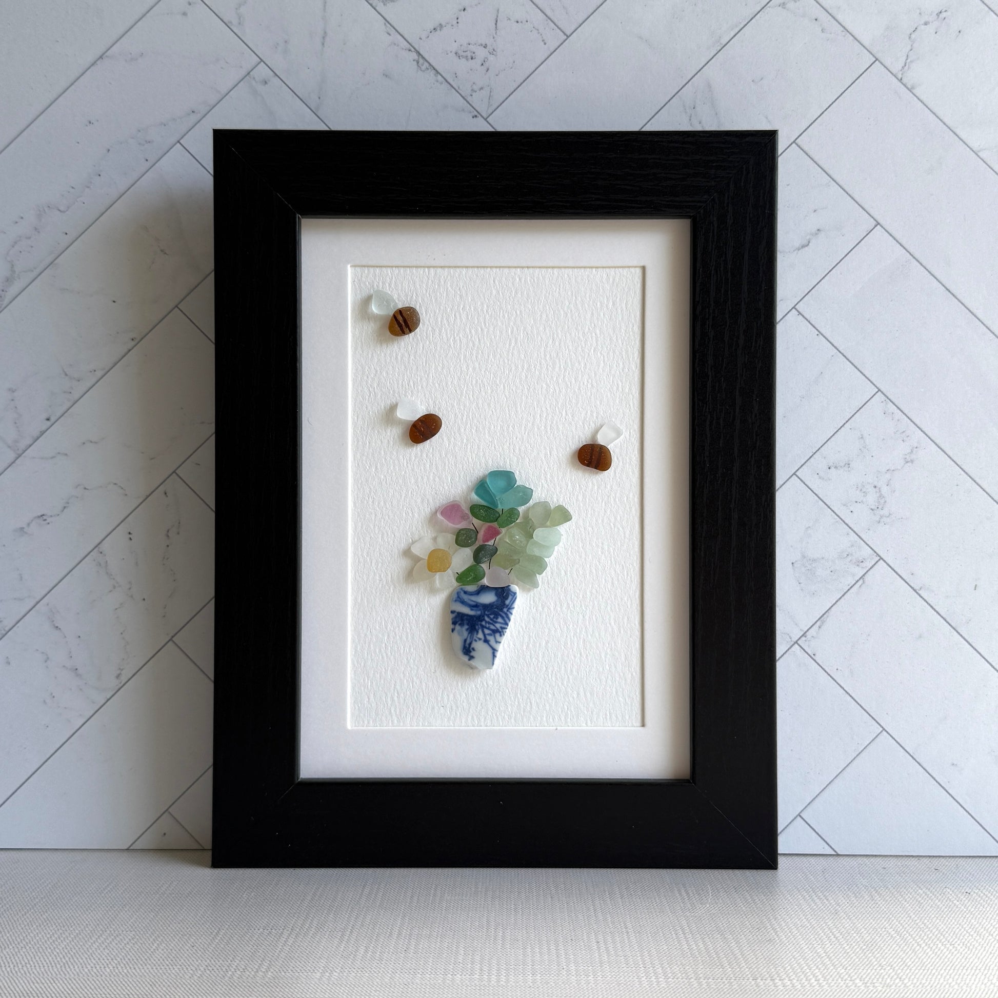 Framed artwork with a floral arrangement made of stones on a white textured background