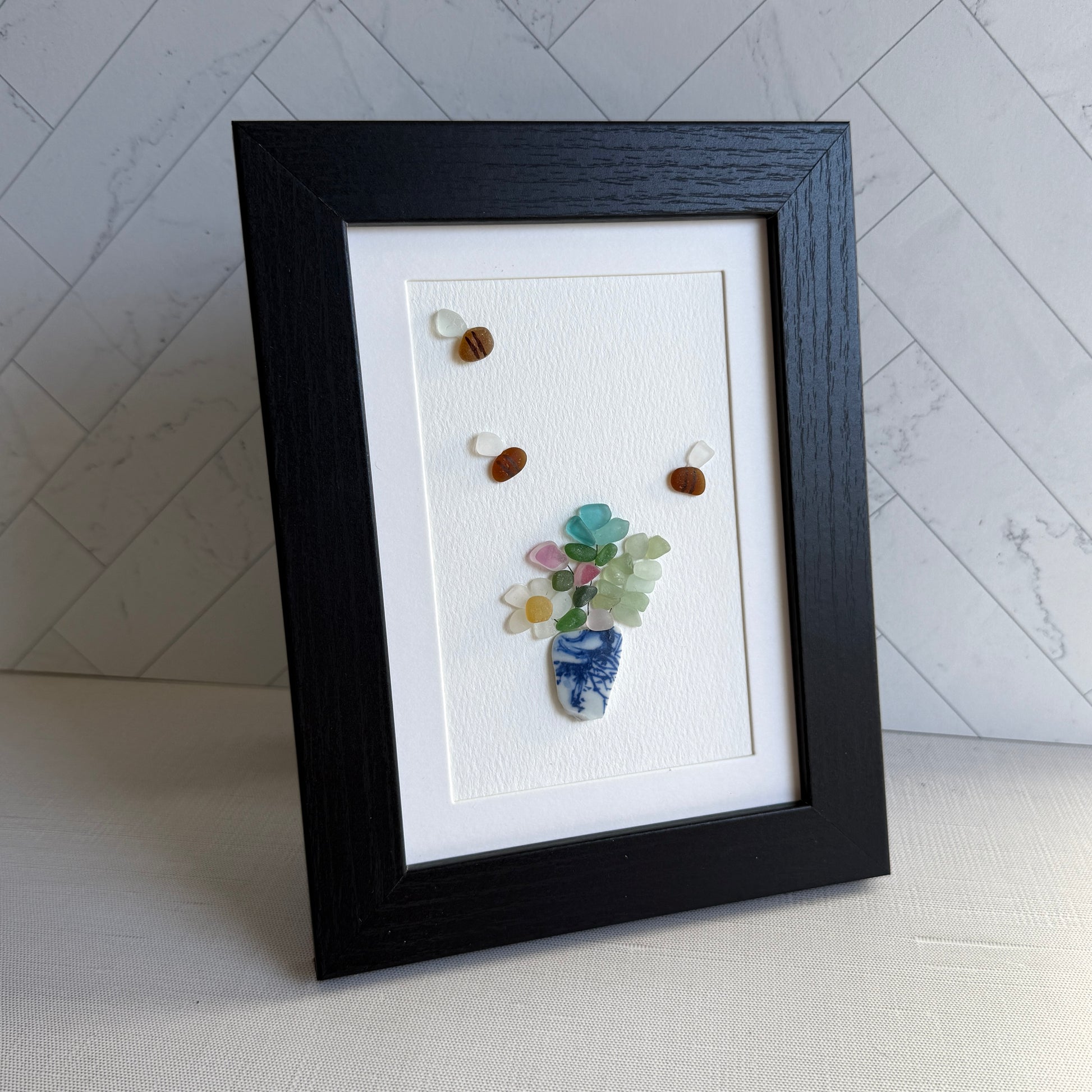 Framed artwork with a vase and flowers made from stones on a white background