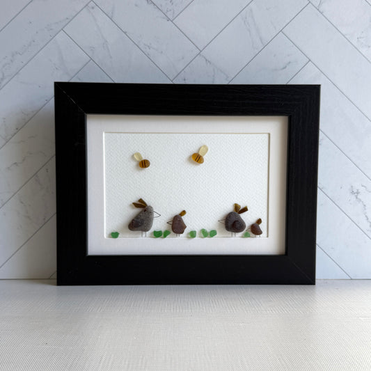 Framed sea glass artwork of hens and chickens on a white background with a black frame.